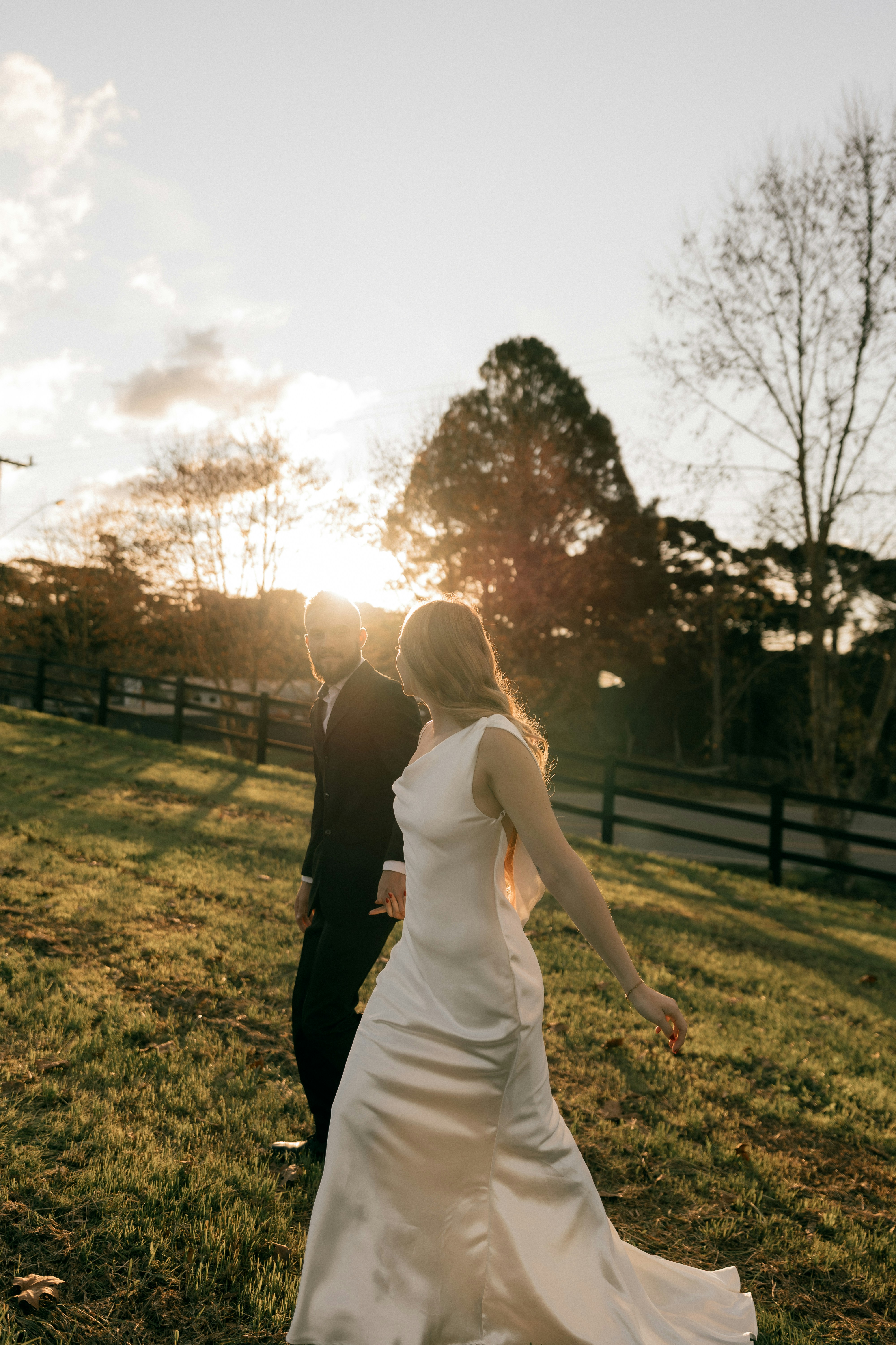 Sposa e sposo che camminano in un campo al tramonto.