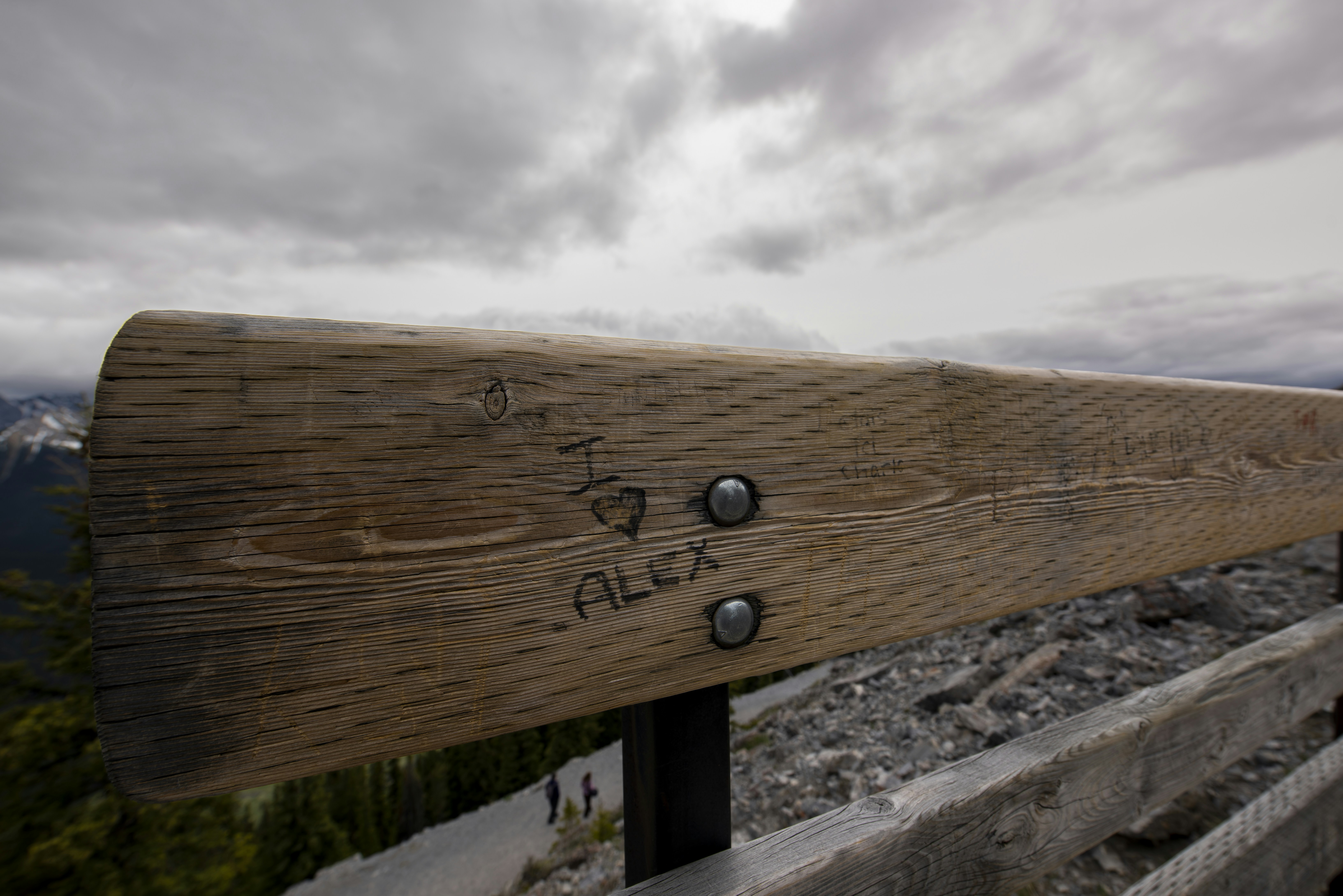 Carved 'alex' on a wooden railing overlooking cloudy mountains