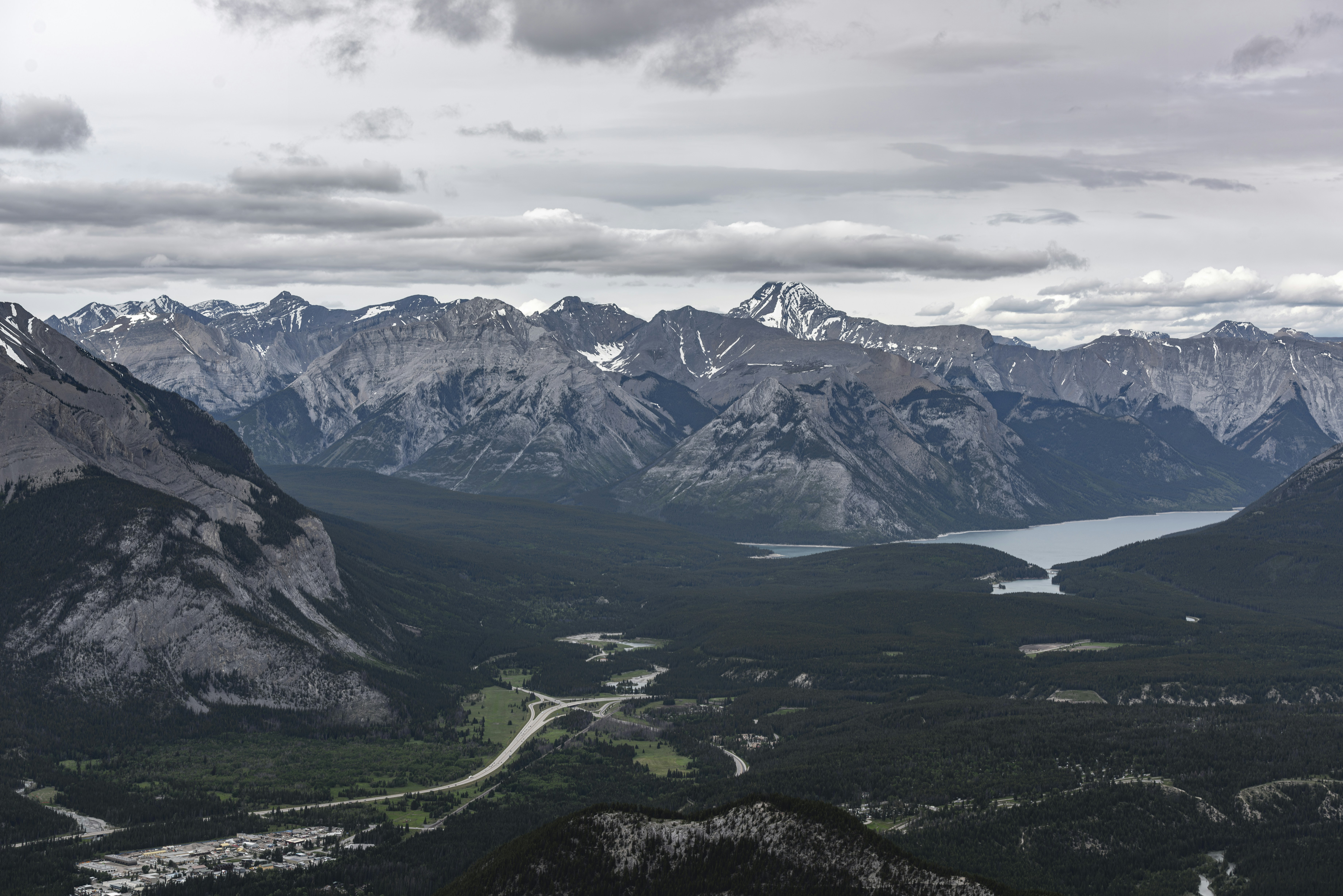 Vast mountain range, valley, lake, and road under cloudy sky