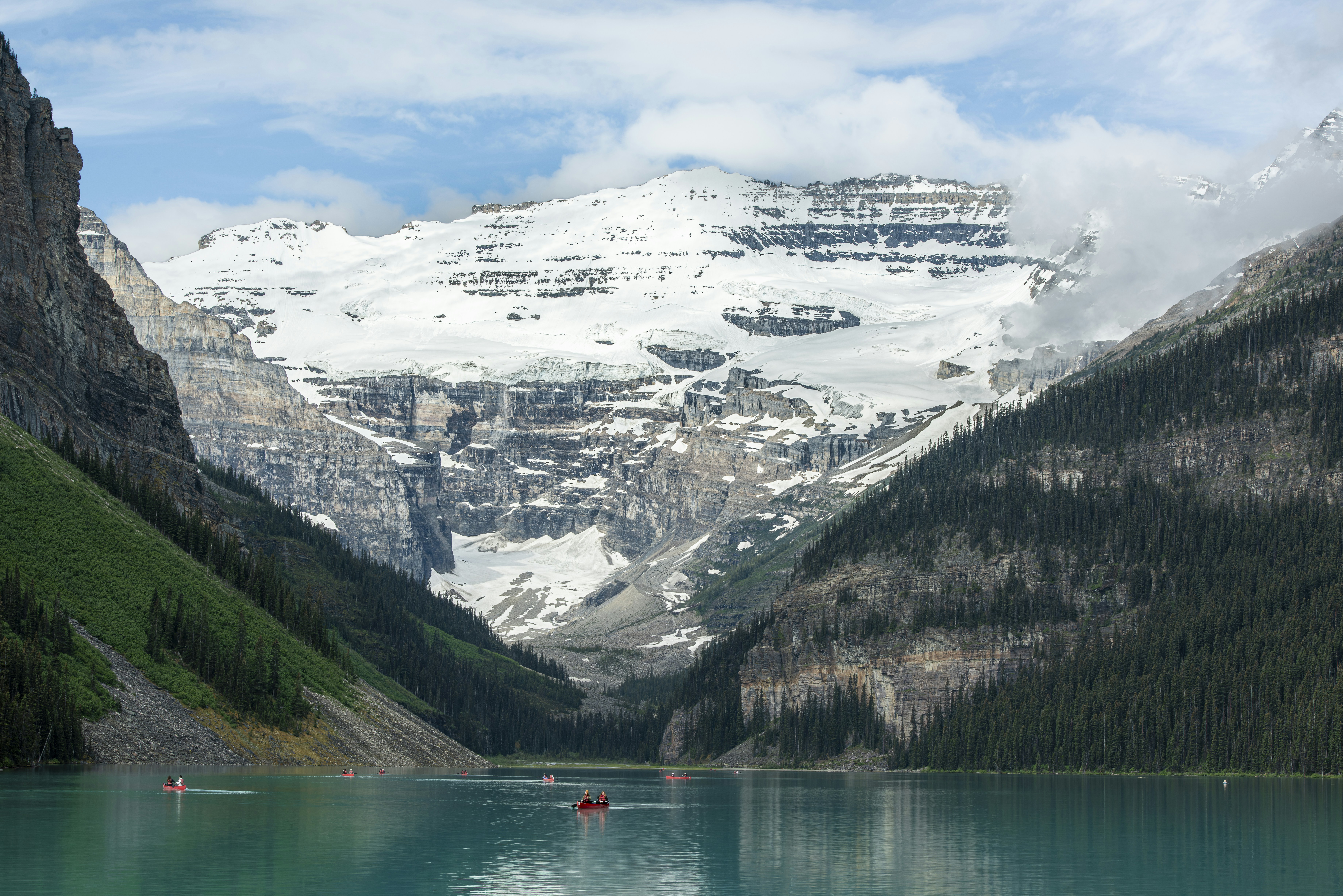 Turquoise lake, canoes, and snow-capped mountains under cloudy sky