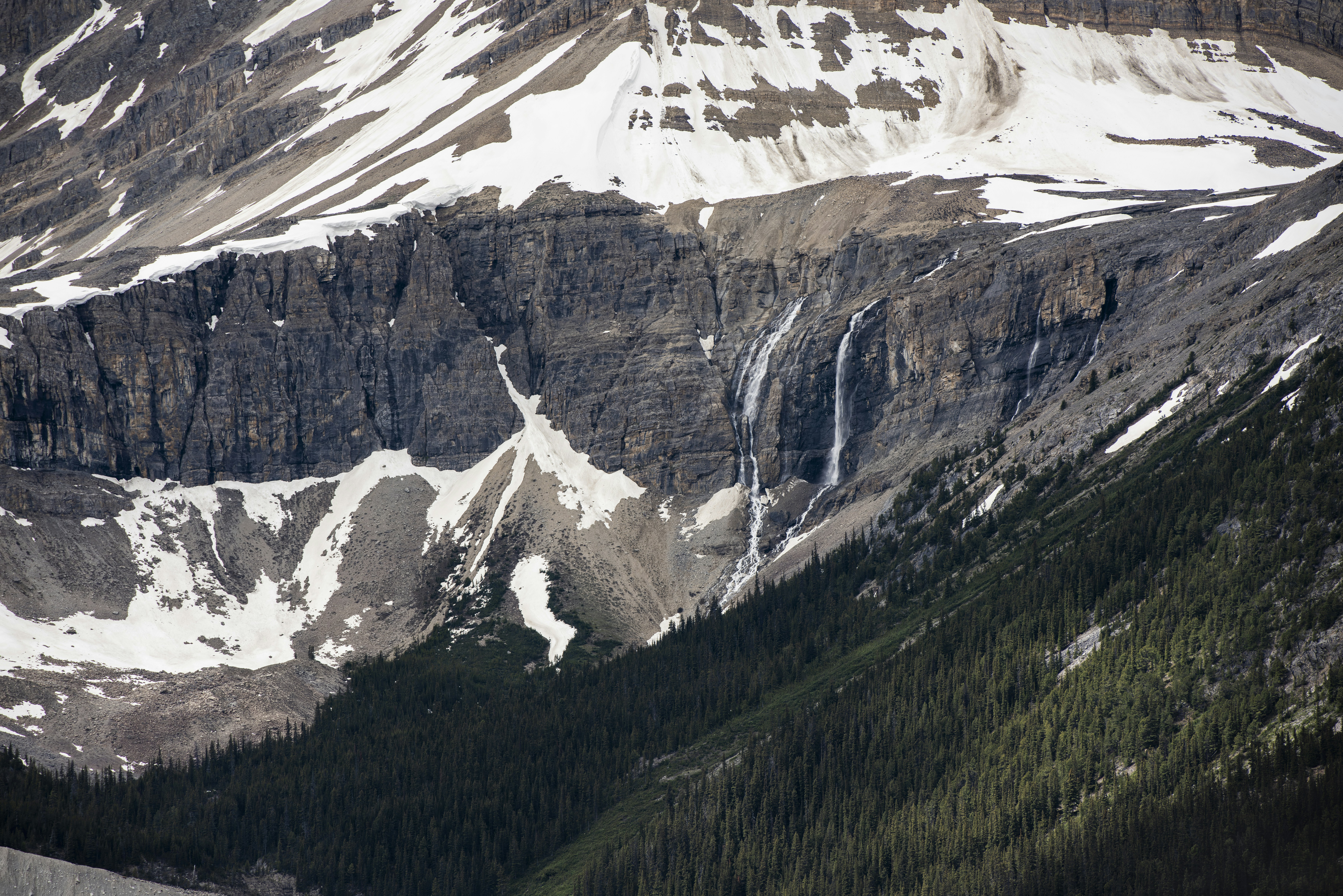 Waterfall flowing down a rocky mountain with snow and trees