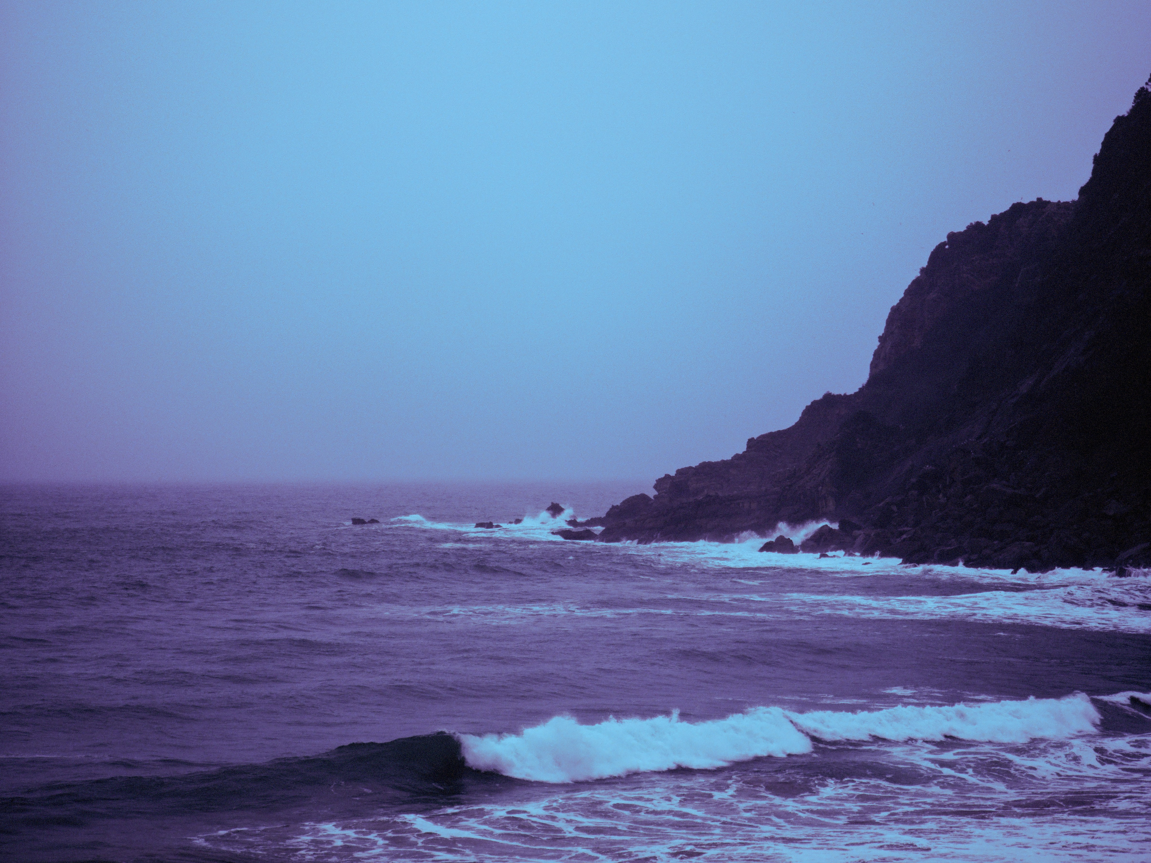 Dark, rocky coastline with waves crashing under a moody sky.