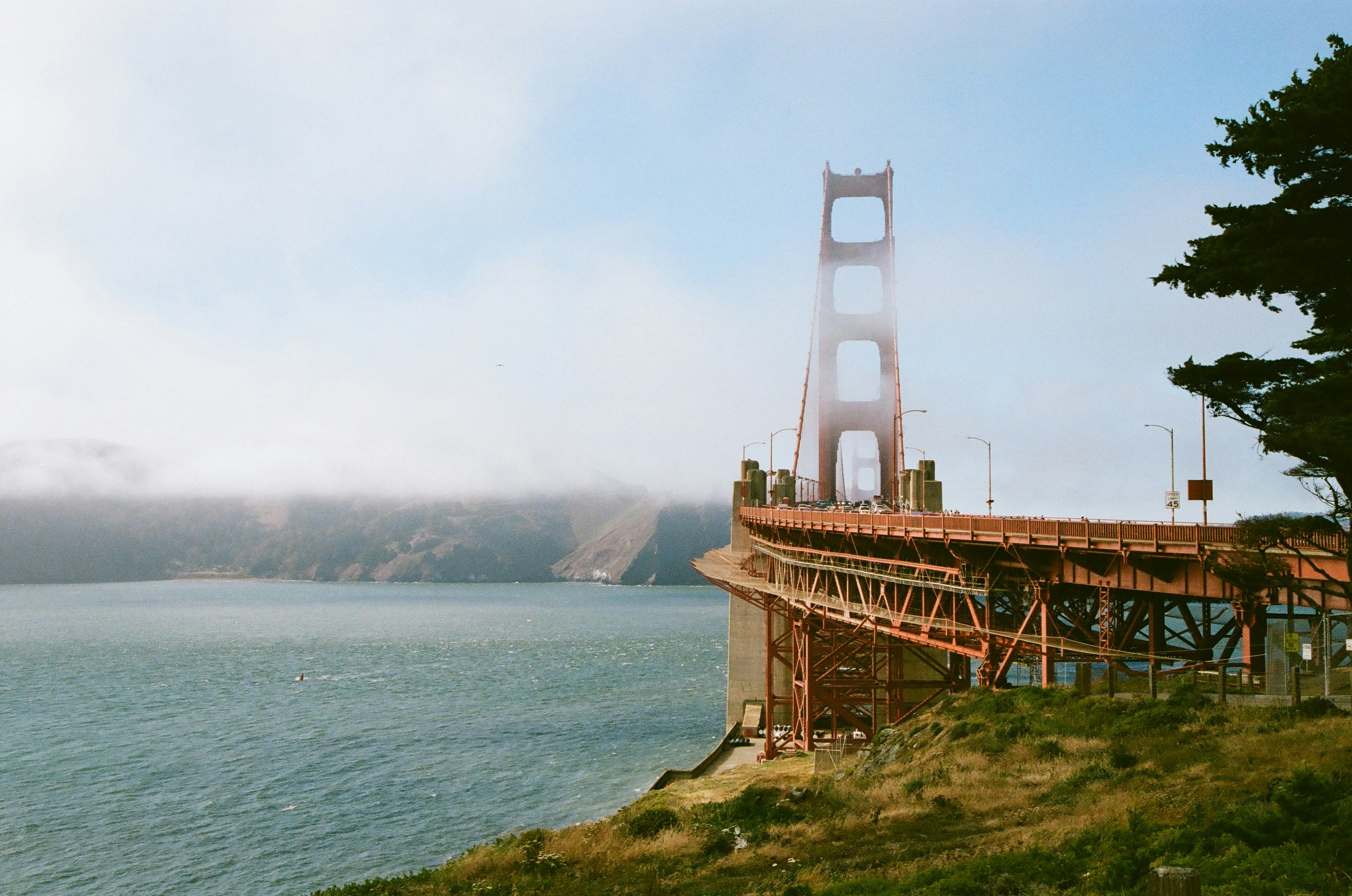 Golden gate bridge partially hidden by fog over blue water.