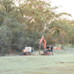 Orange excavator, utility truck, and workers in a grassy field