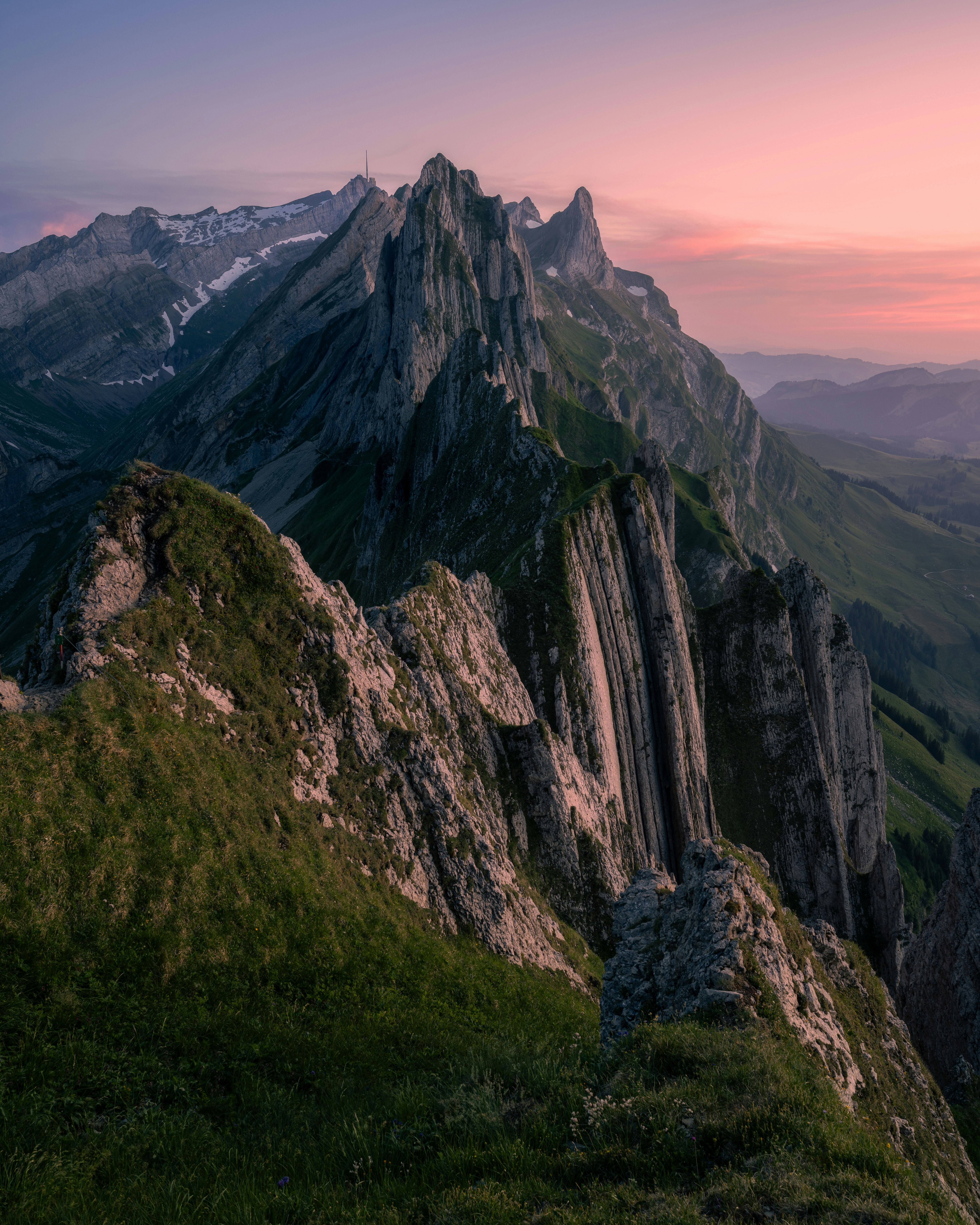 Dramatic mountain peaks and green slopes at sunset.