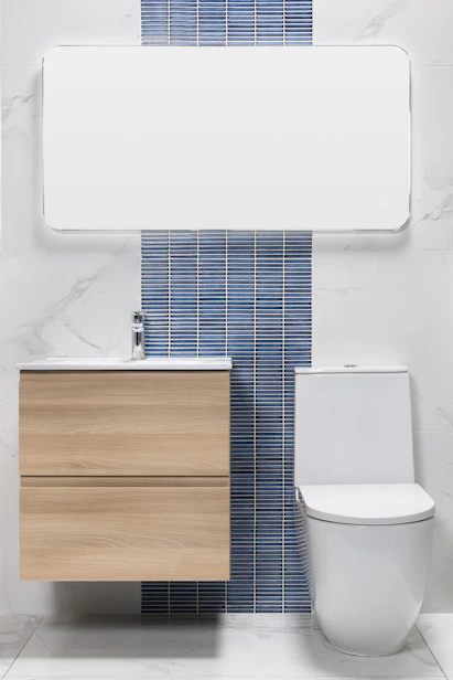 A modern bathroom with a mirror, wooden vanity, and toilet.