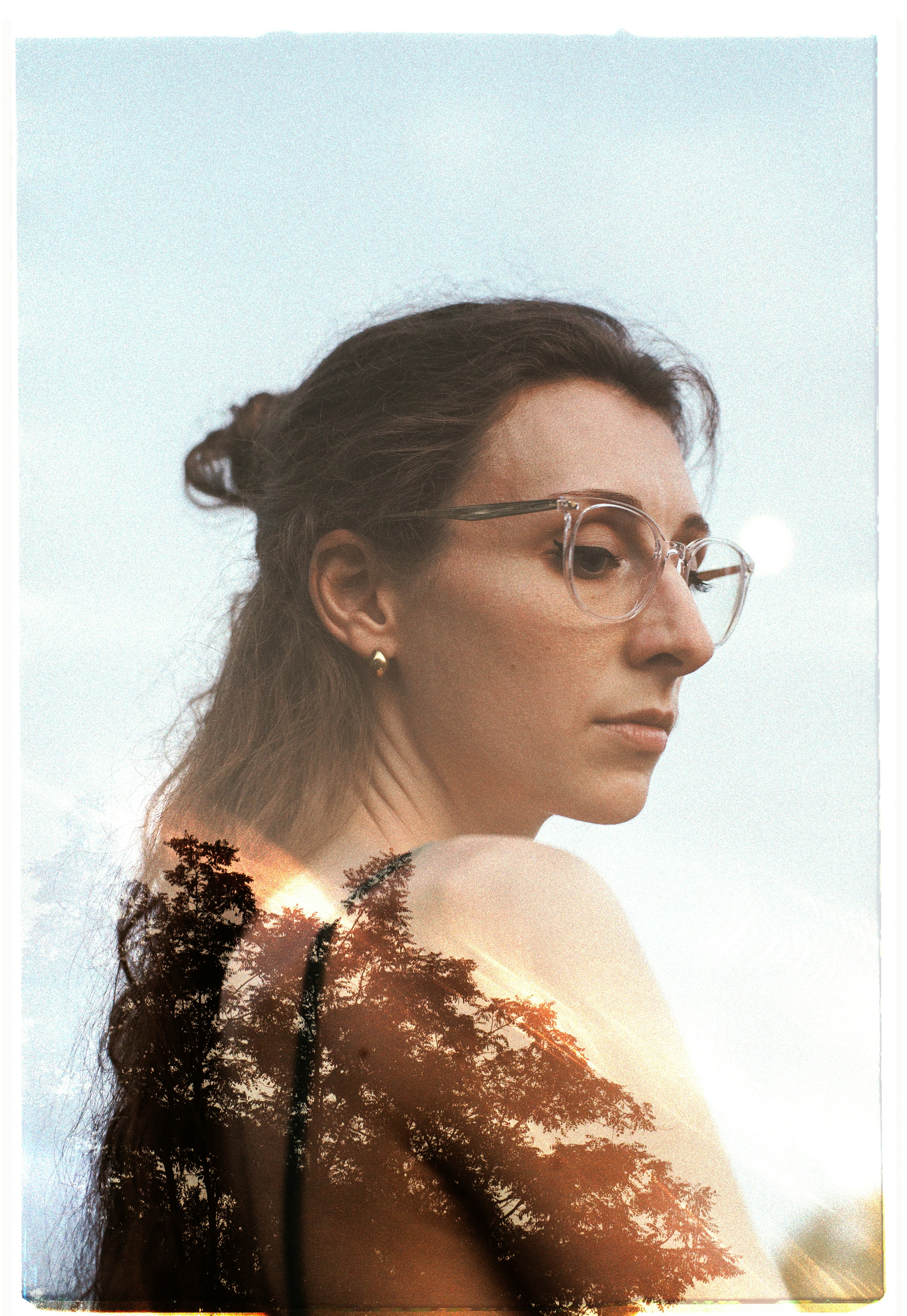 Double exposure of a woman with glasses and sunlit trees.