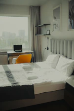 Modern bedroom featuring a bed, desk, laptop, and window.