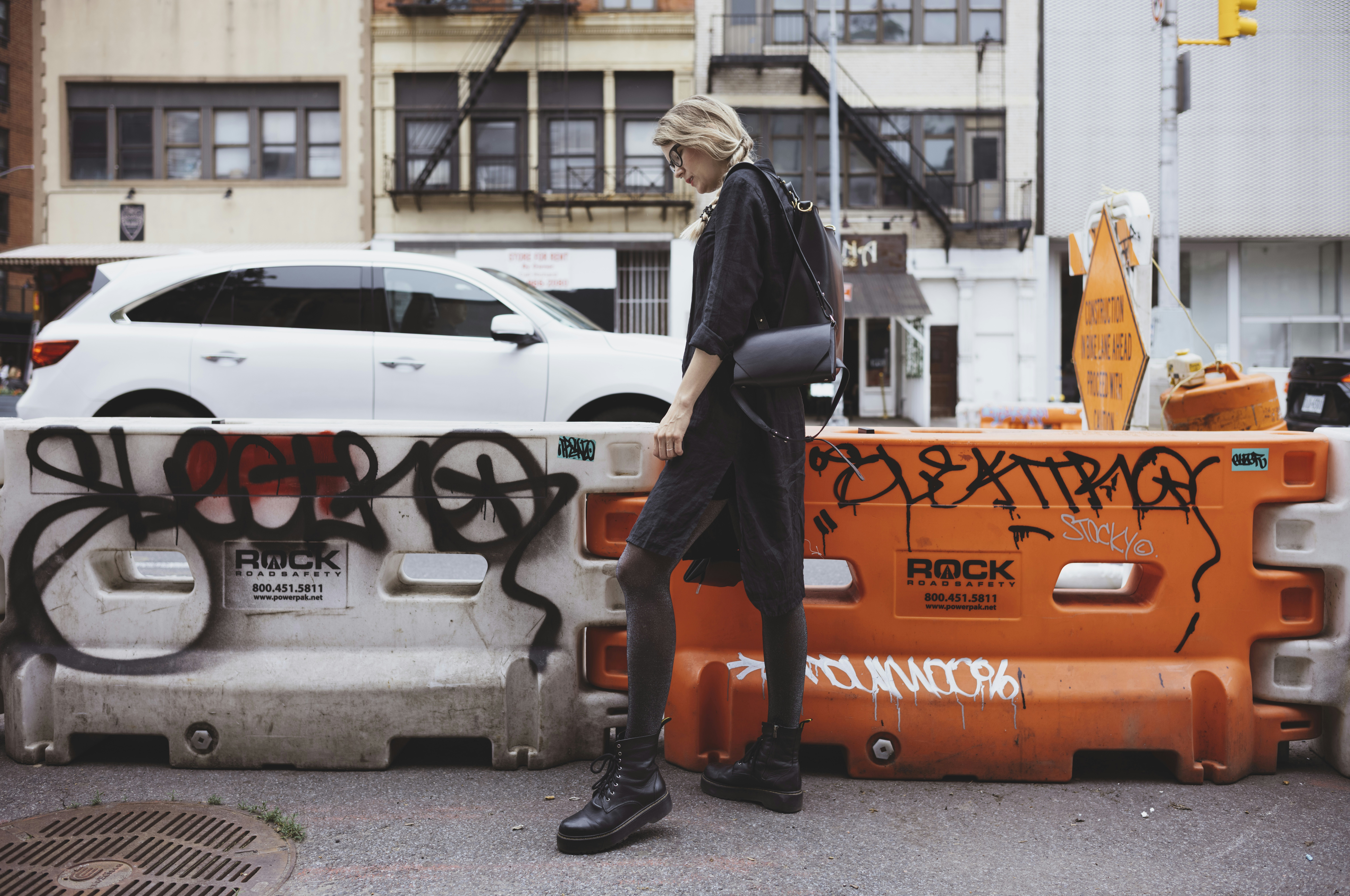 Woman in dark clothing walks past graffiti barriers.