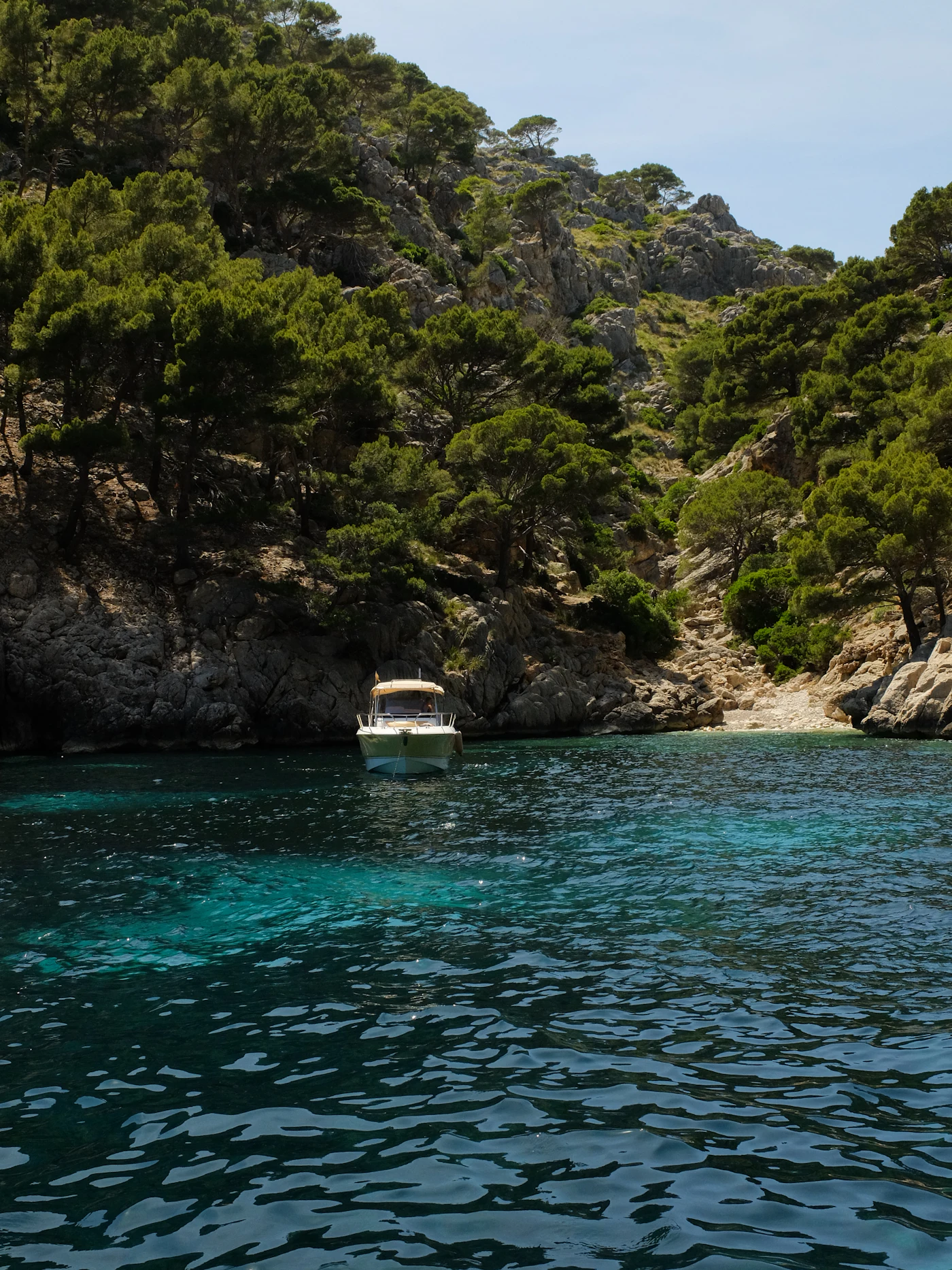A small white boat lying in a sheltered turquoise cove enclosed by green wooded hills.