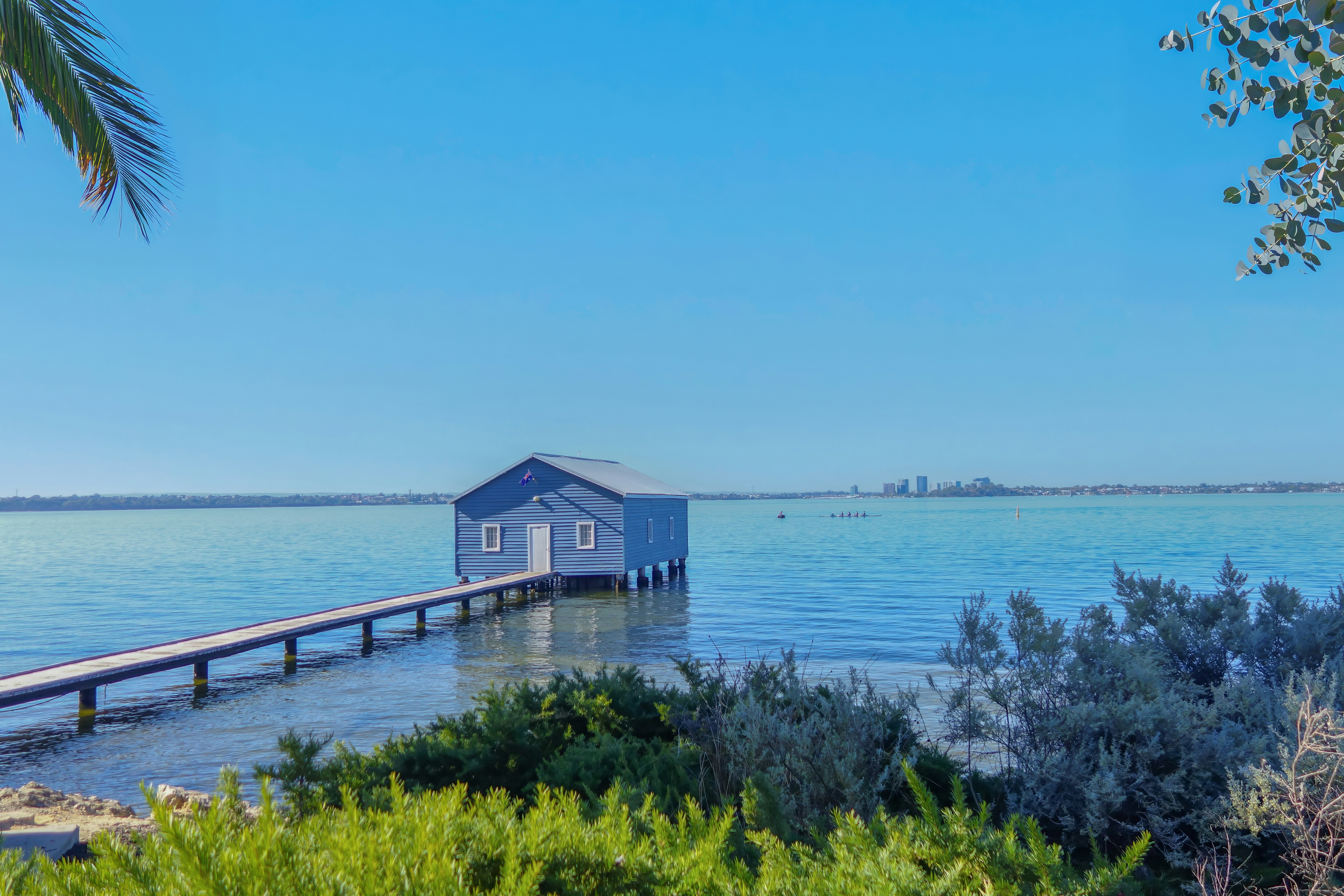 Blue boathouse and jetty extending into calm, clear water.