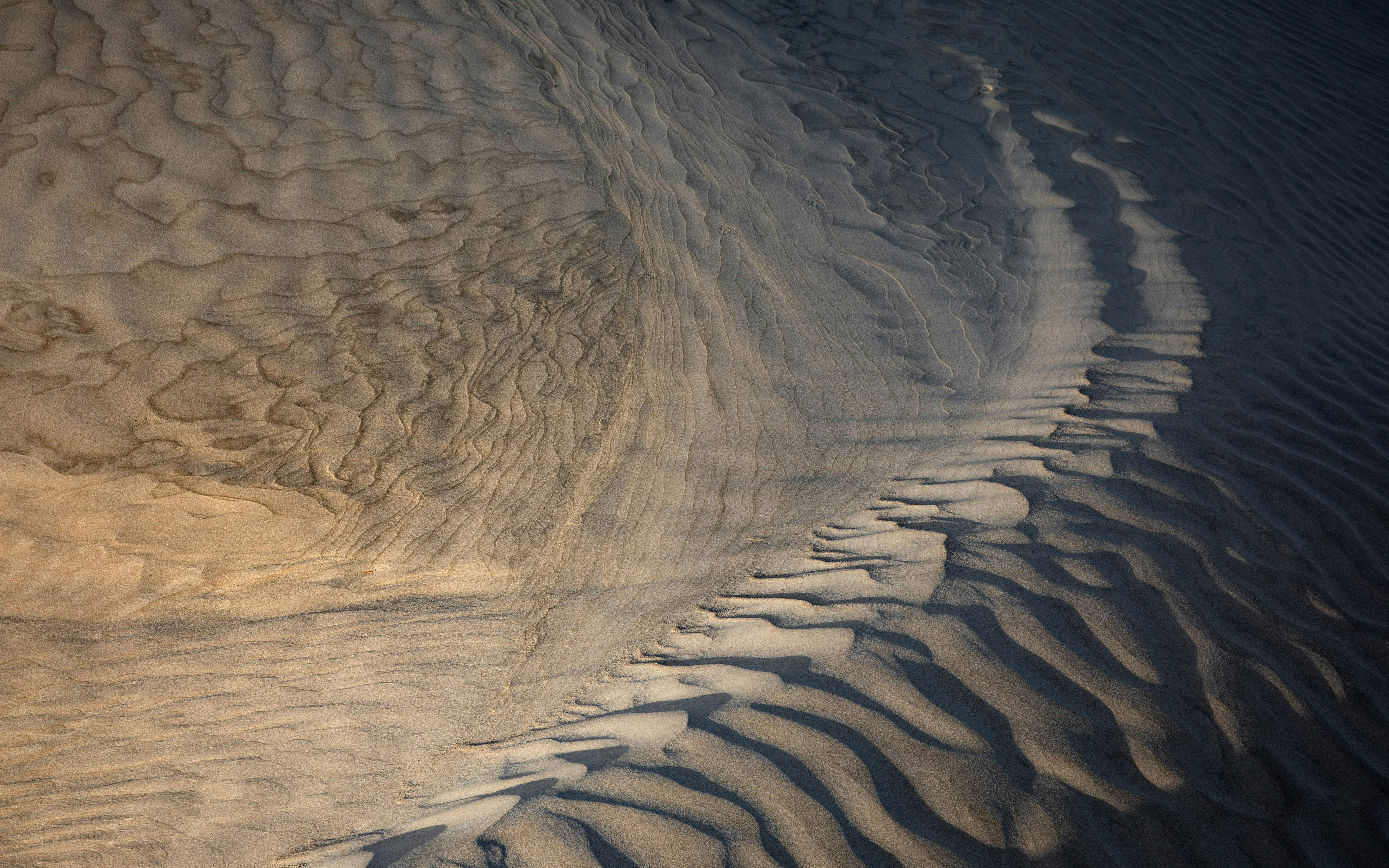 Abstract view of sand dunes with intricate ripples and shadows.