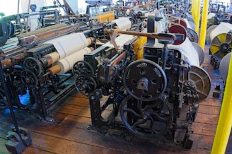 Old industrial weaving machines with fabric rolls in a factory.