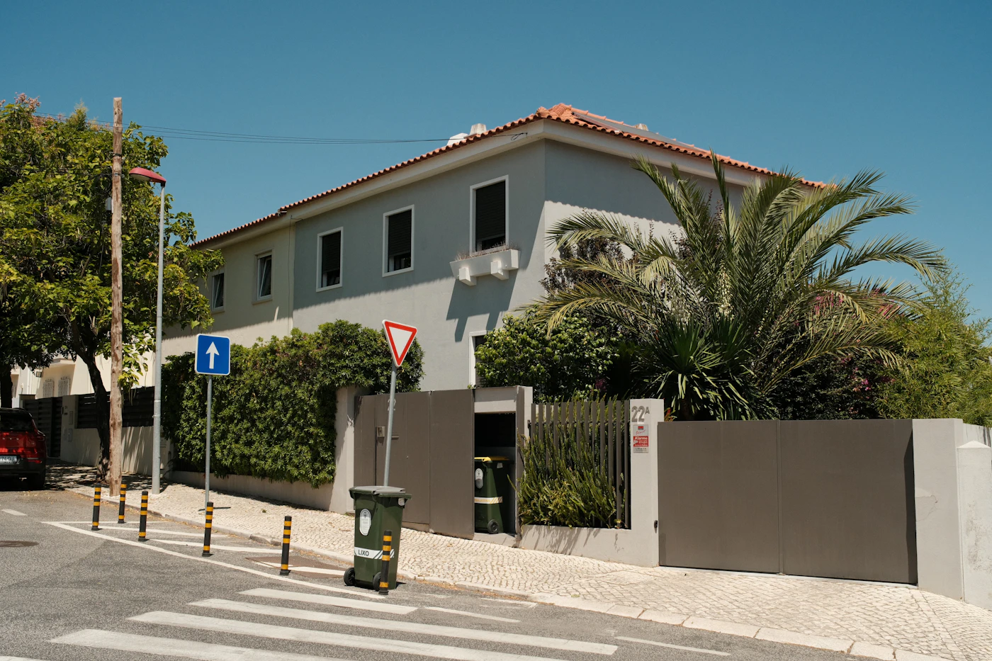 A gray house with a terracotta roof, palm trees and a garden on a sunny street in Benfica, Lisbon.