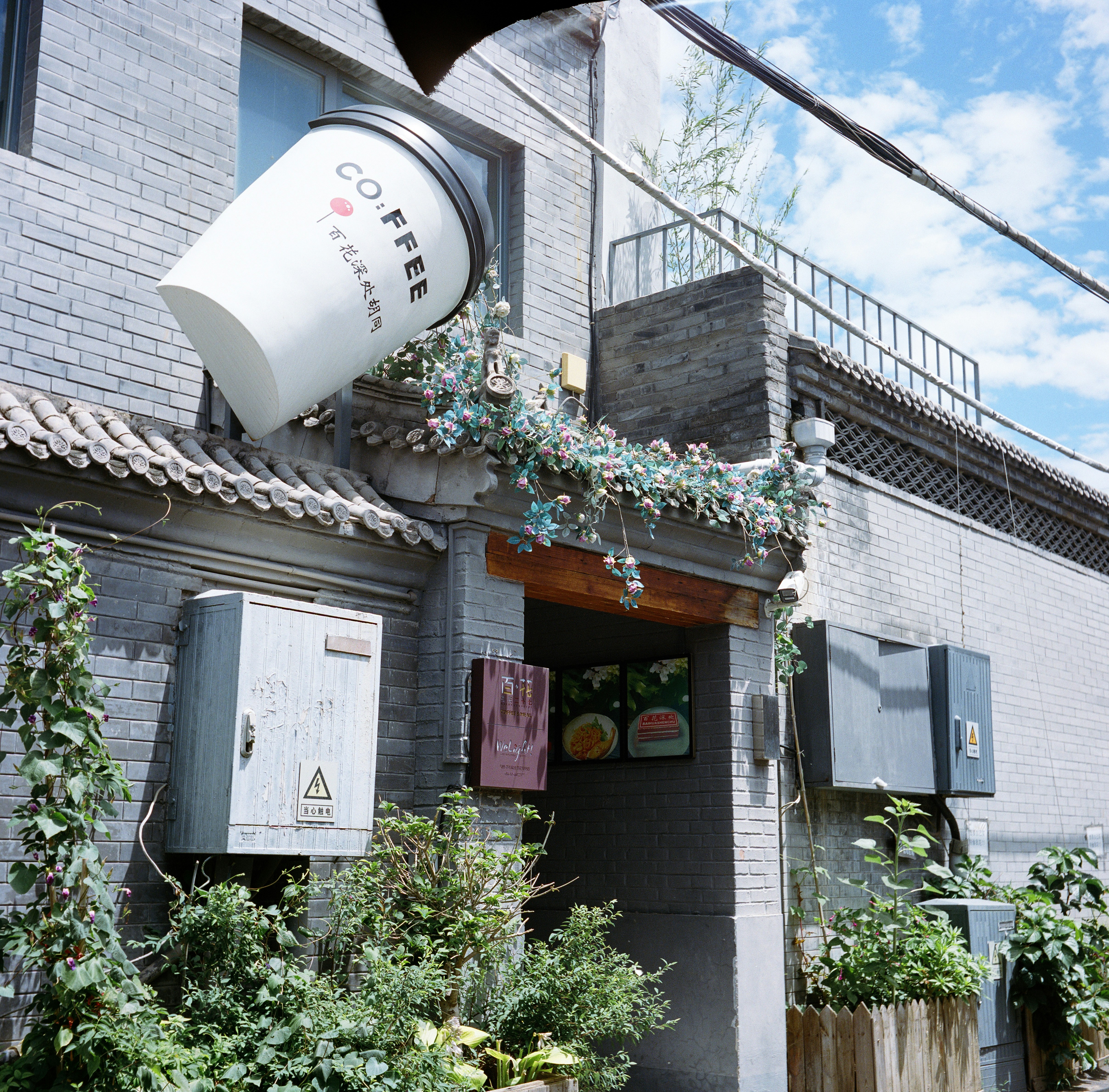 Coffee cup sign on a building with lush green plants.