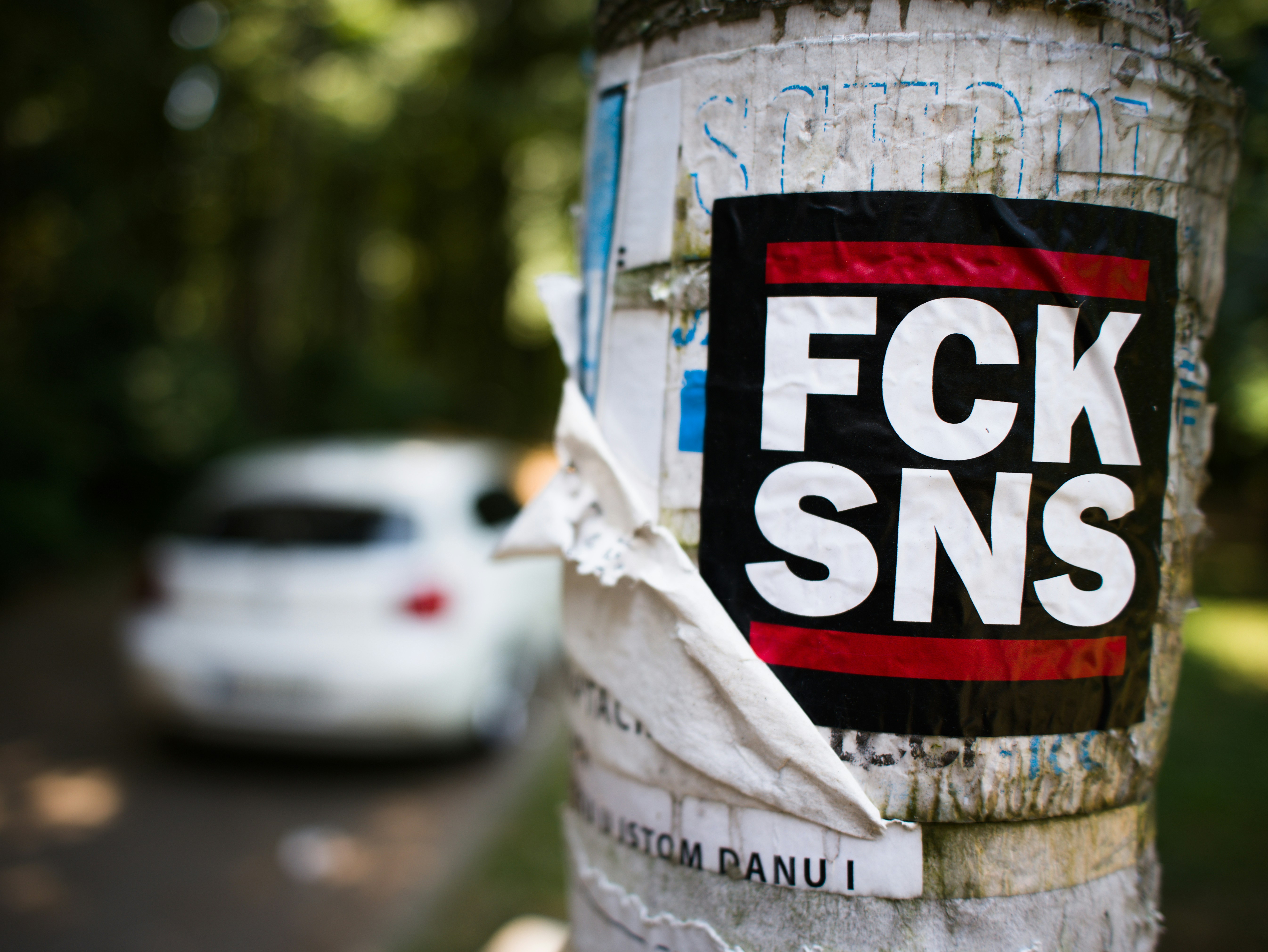 部分的に剥がれた「fck sns」のシールが貼られたポール。