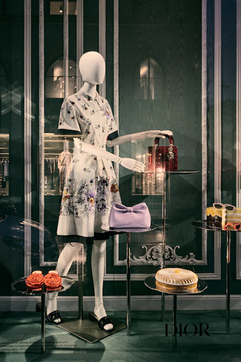 Mannequin in floral dress, designer bags, and pastries.