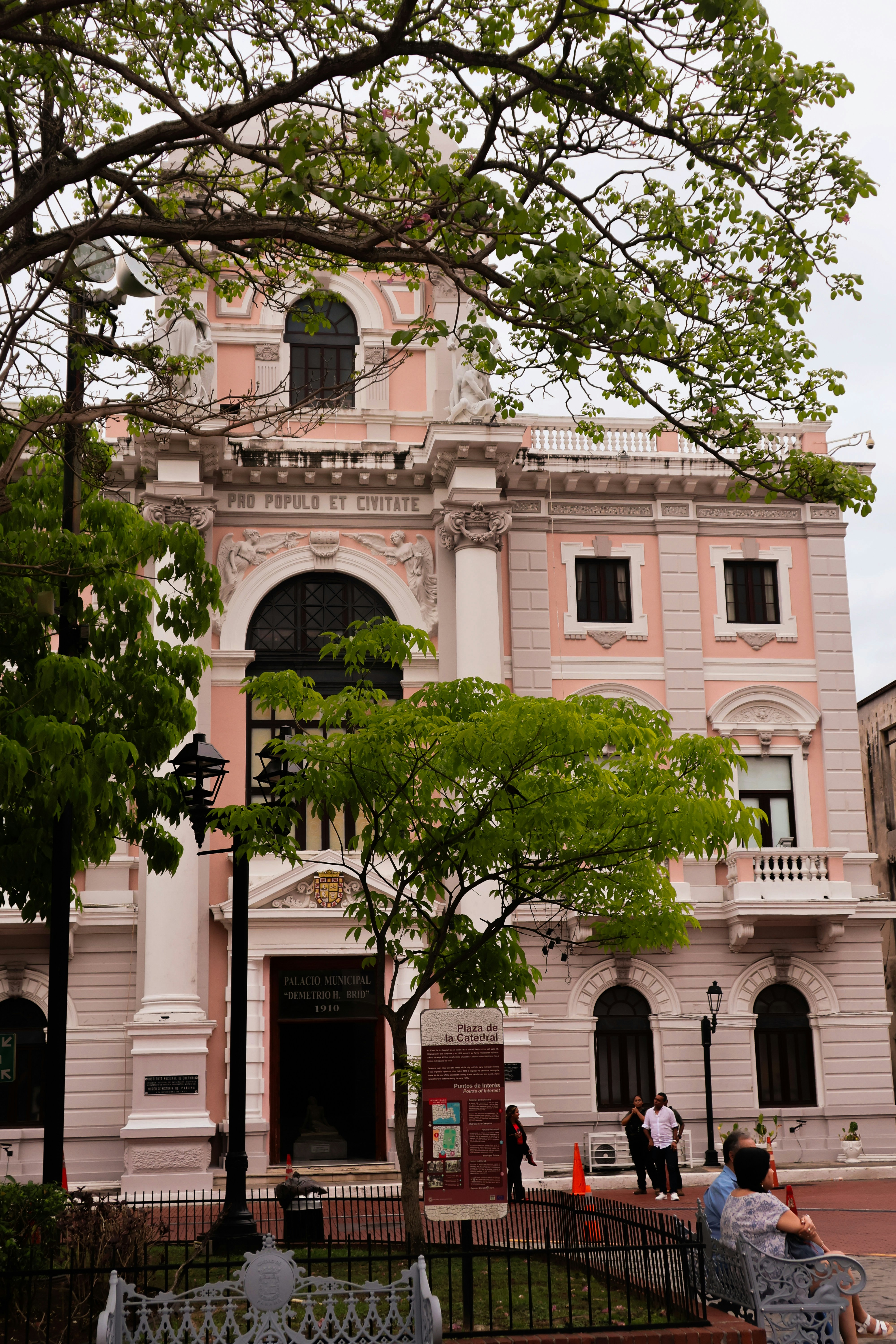 Ornate pink building with trees in an urban square.