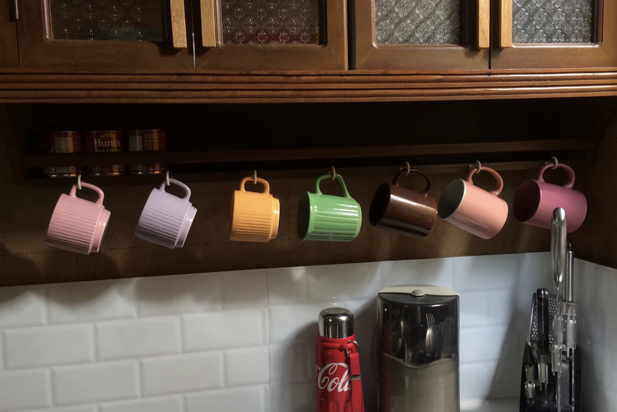 Mugs hanging on hooks under a small kitchen shelf