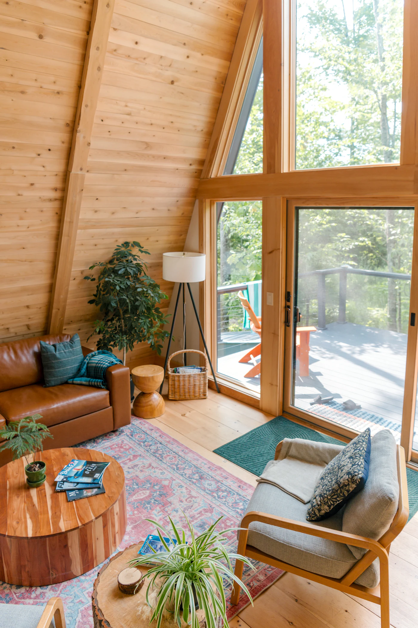 Living room with tall windows looking out on trees, a wood stove and warm wood finishes