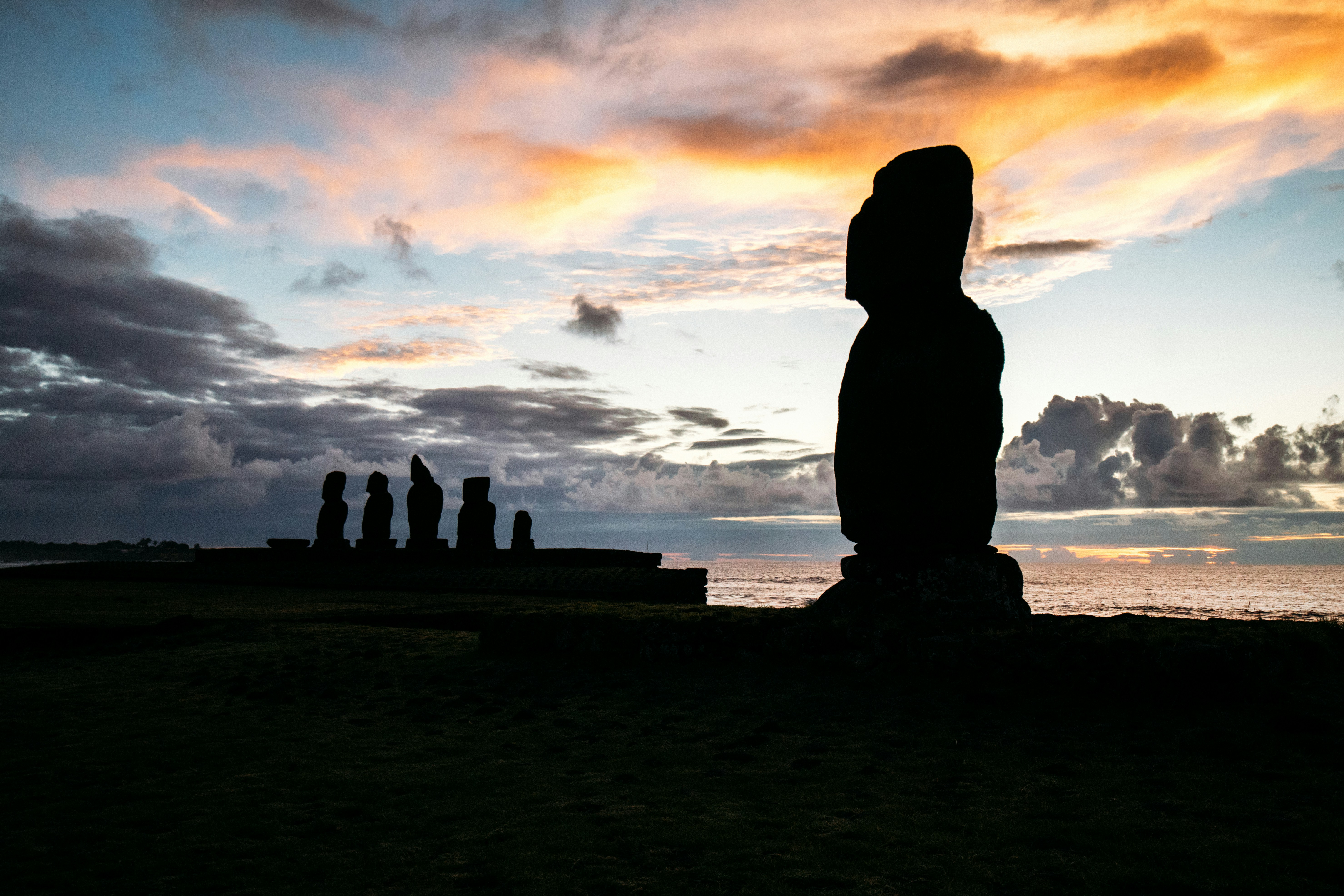 Ancient moai statues silhouetted against a dramatic sunset.