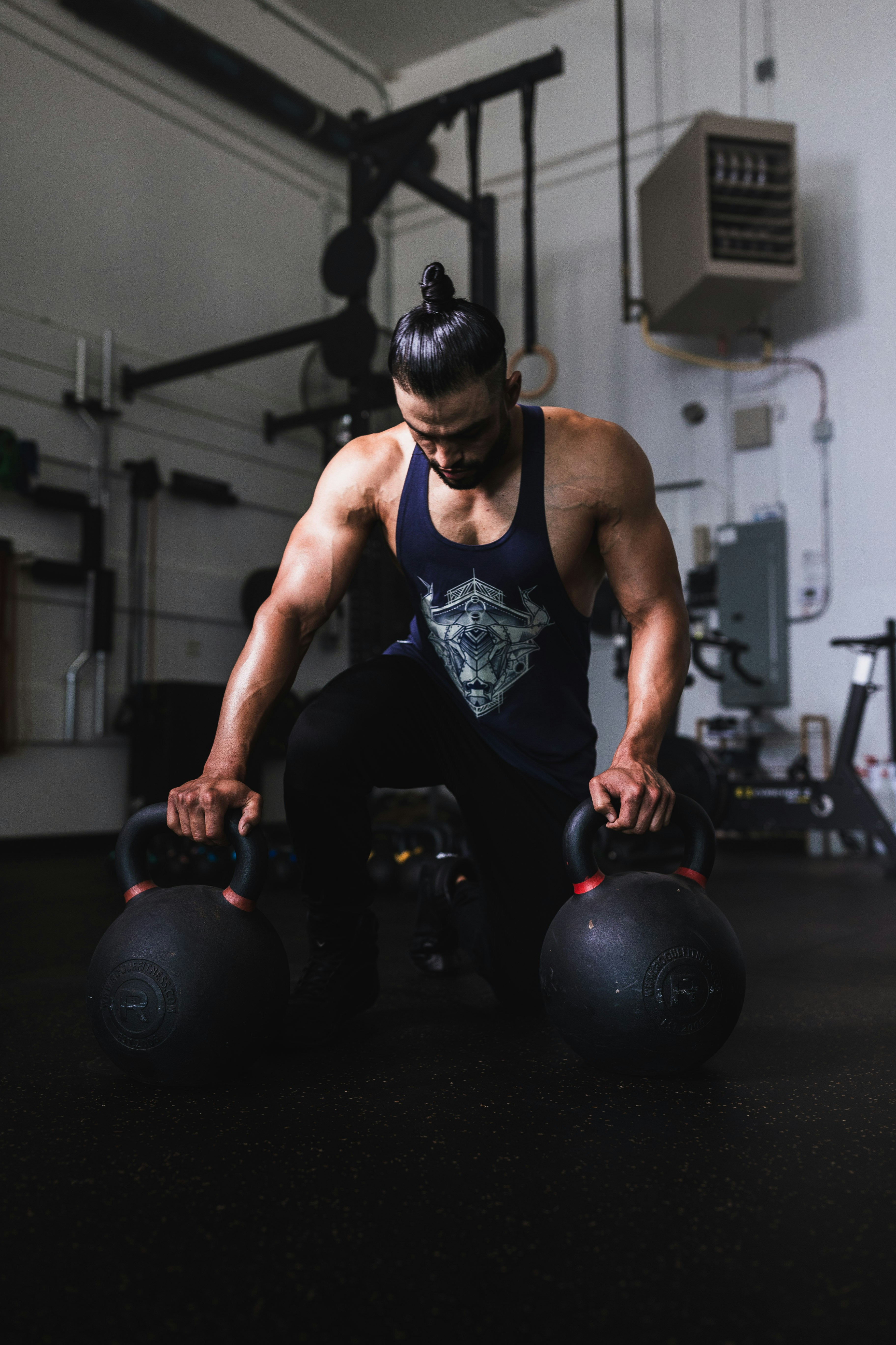 Athlète tenant de lourdes kettlebells dans une salle de sport sombre