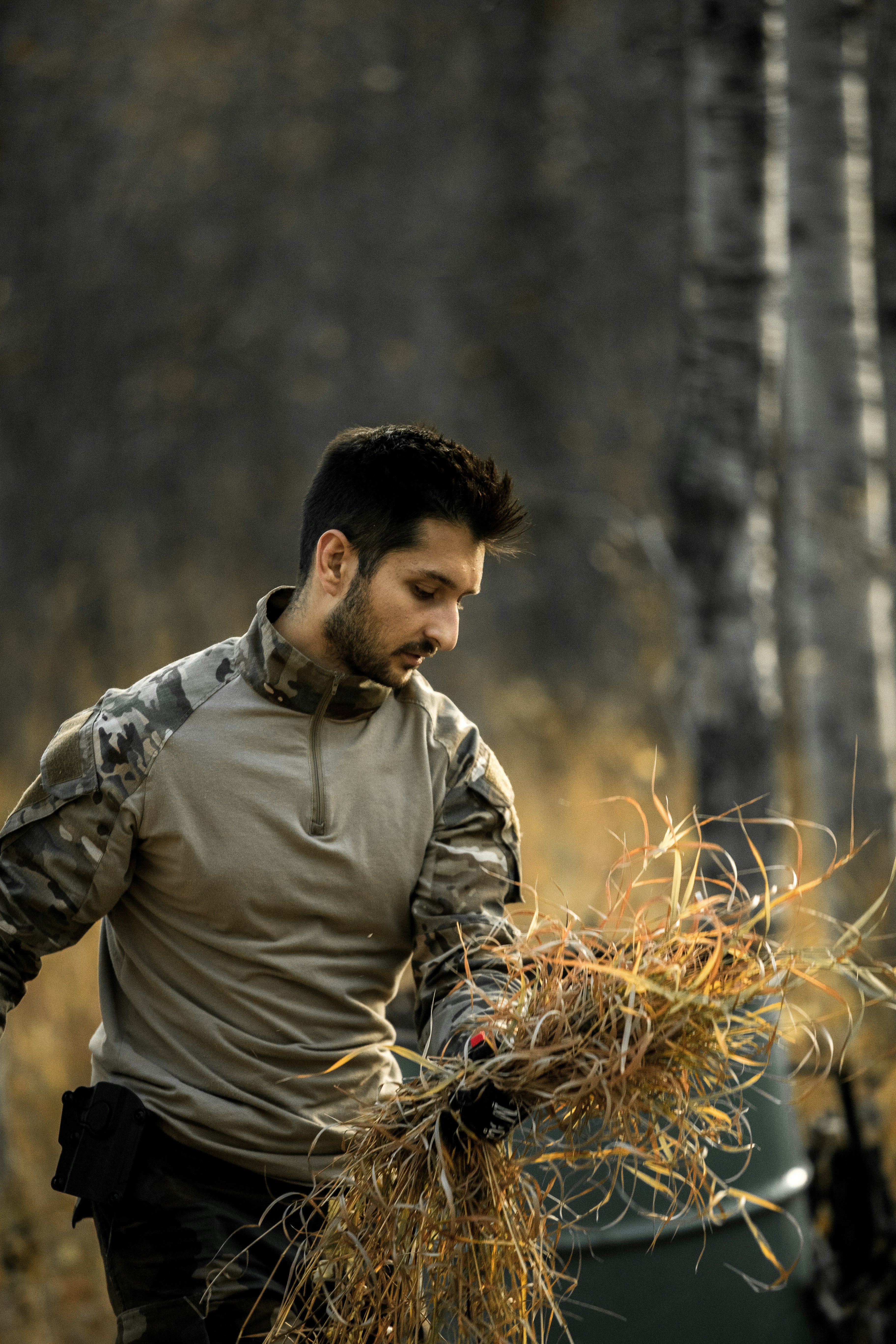 Homme en chemise tactique ramasser de l’herbe sèche dans la nature
