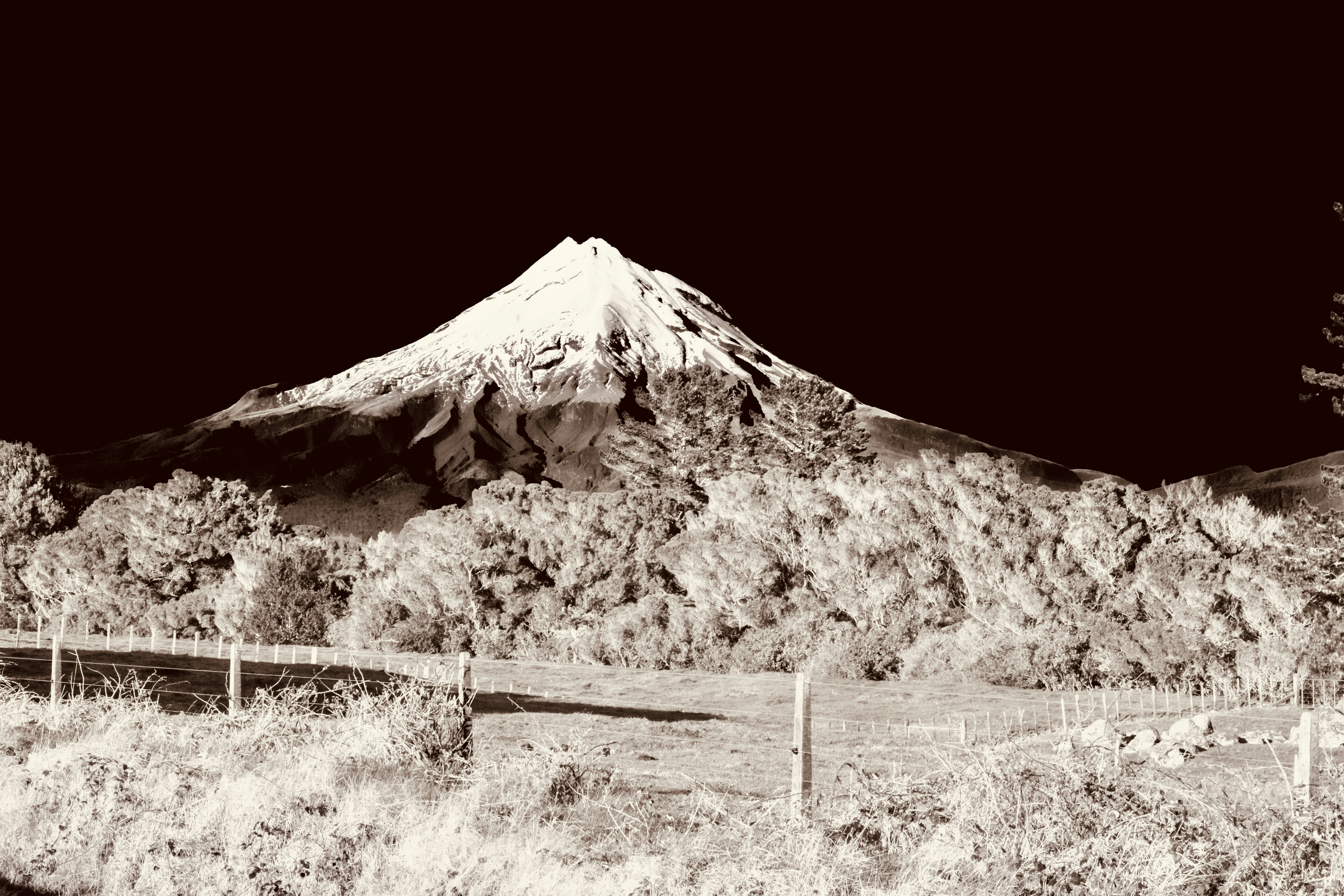 Dramatic snow-capped mountain and fence under a dark sky.