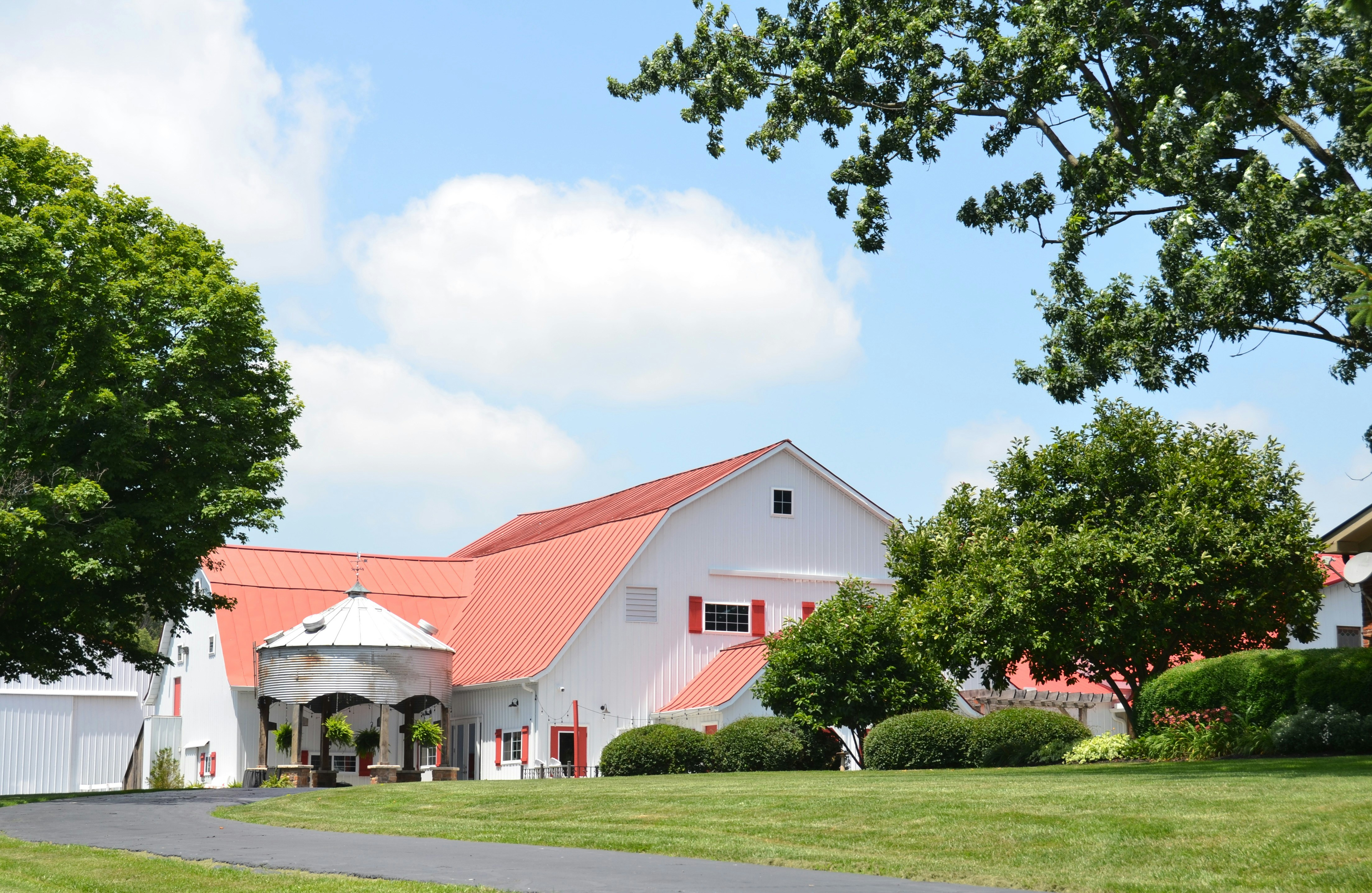 White barn with red roof, green trees, and grassy lawn.