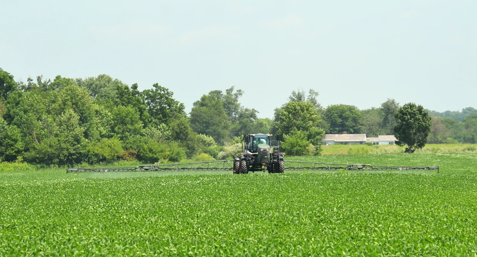 Tractor with a boom sprayer applying liquid fertiliser to a green crop field on a commercial farm
