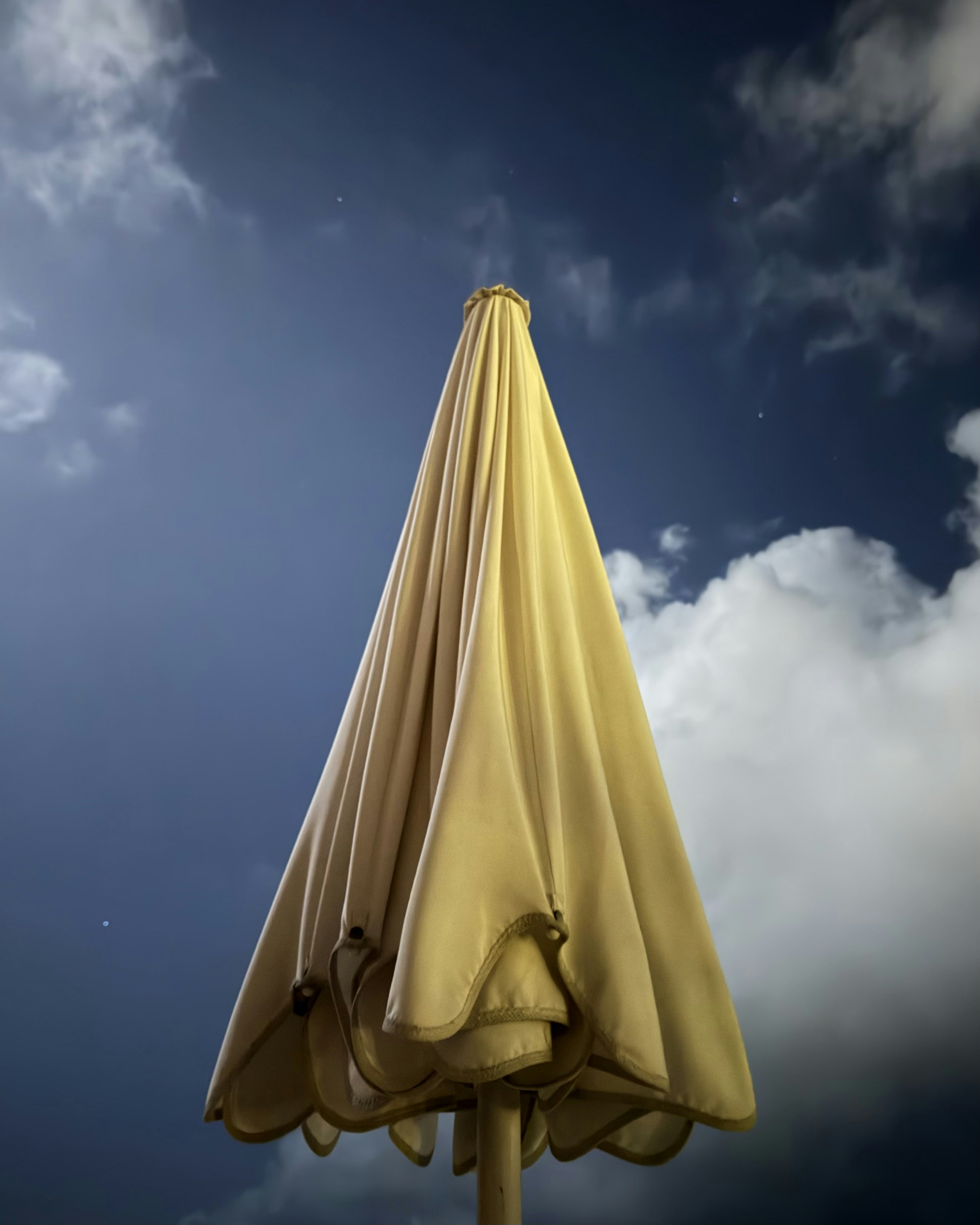 Guarda-chuva amarelo fechado sob um céu nublado e dramático.