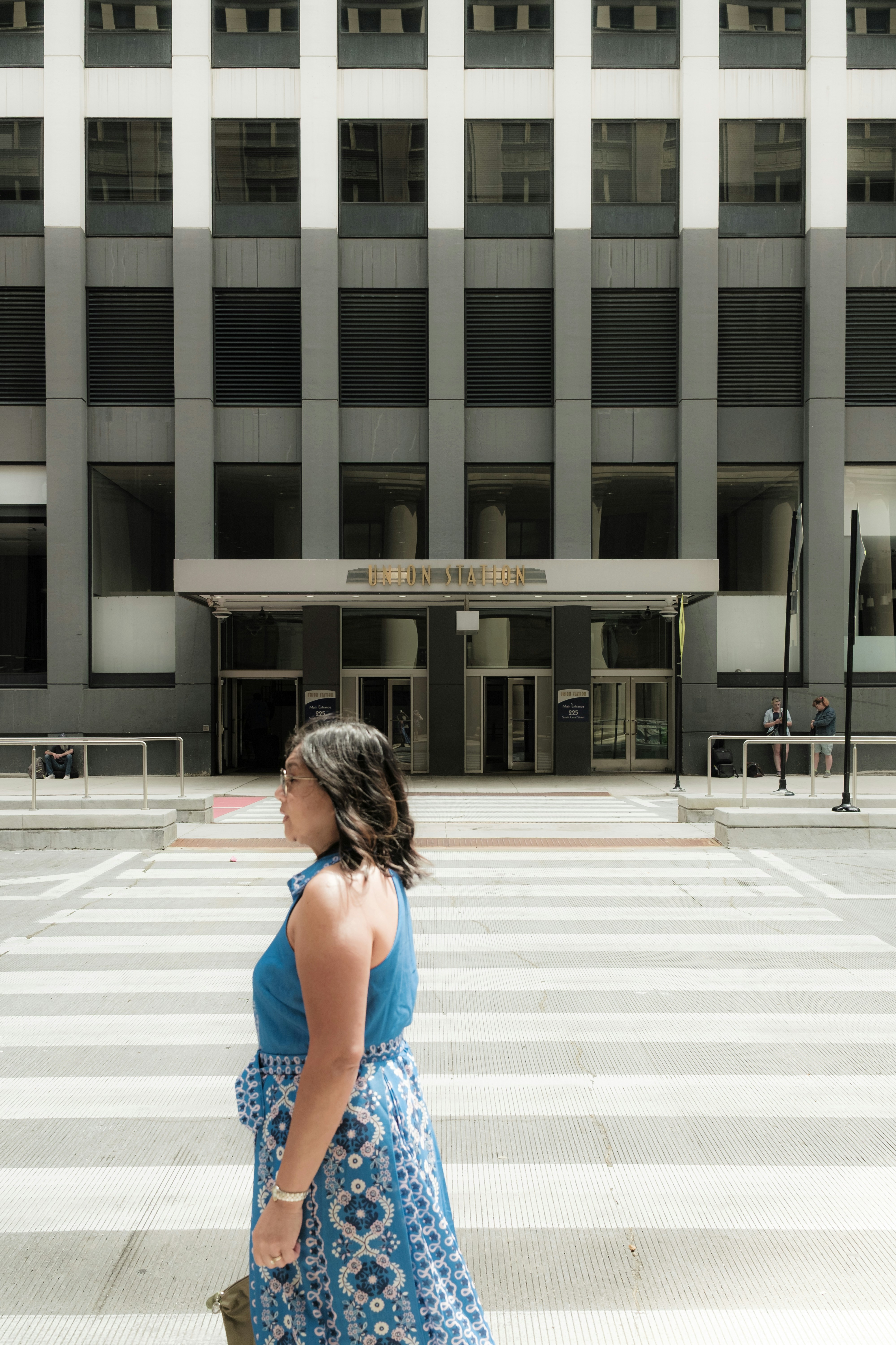 Donna in abito blu attraversa l'attraversamento pedonale vicino a un edificio moderno.