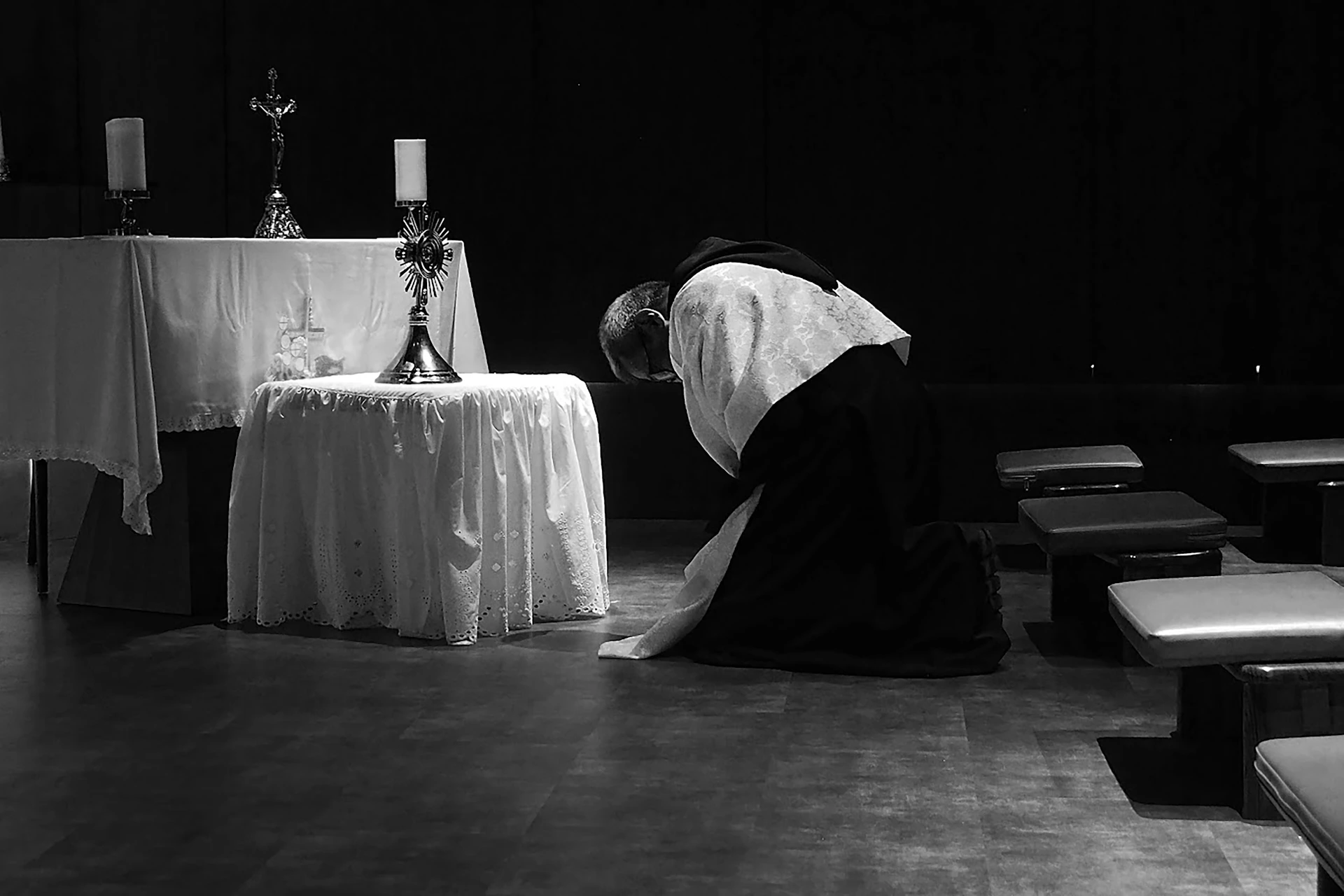 Monk bowing solemnly before an altar with candles.