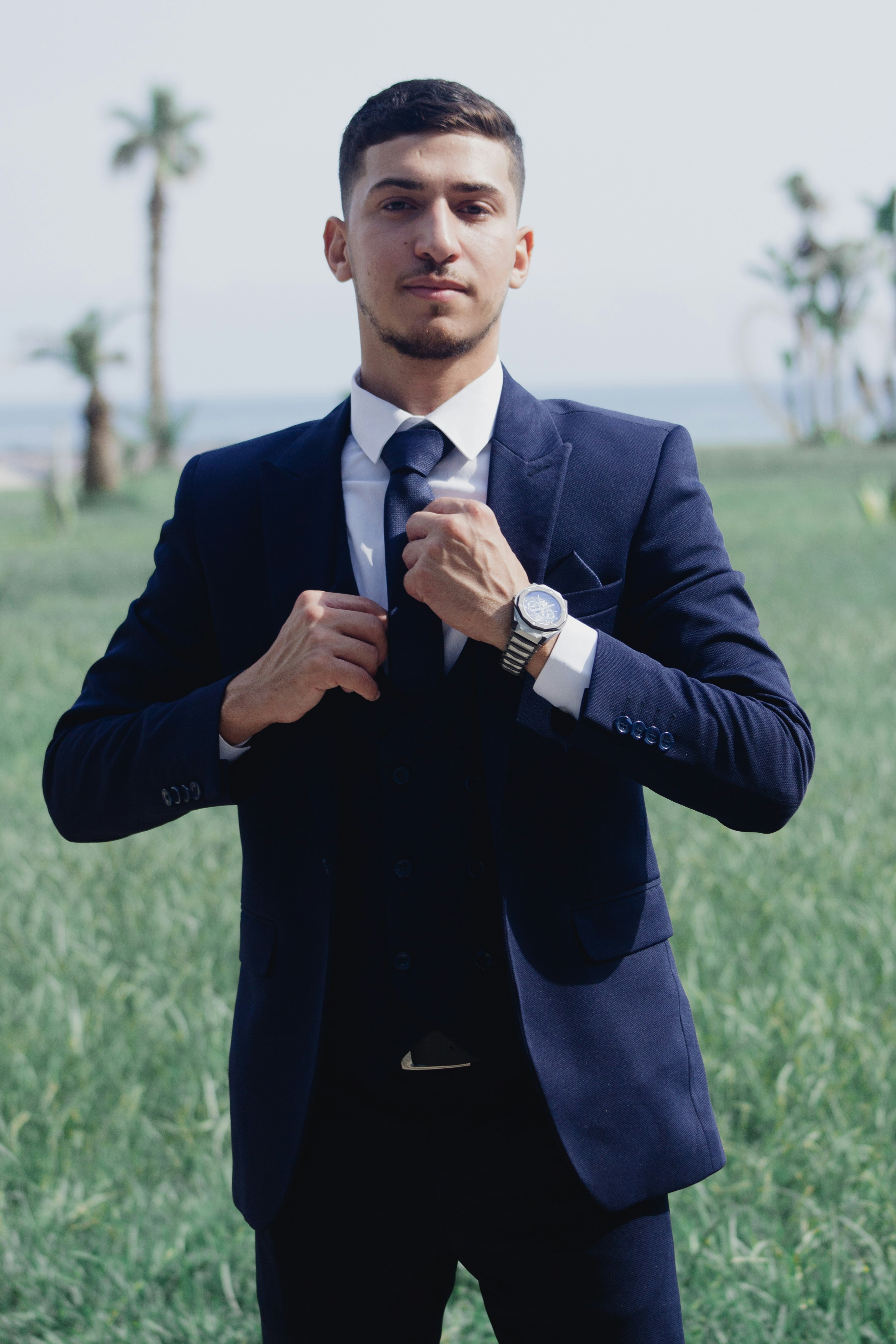 A young man in a suit adjusts his tie outdoors
