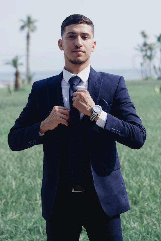 A young man in a suit adjusts his tie outdoors
