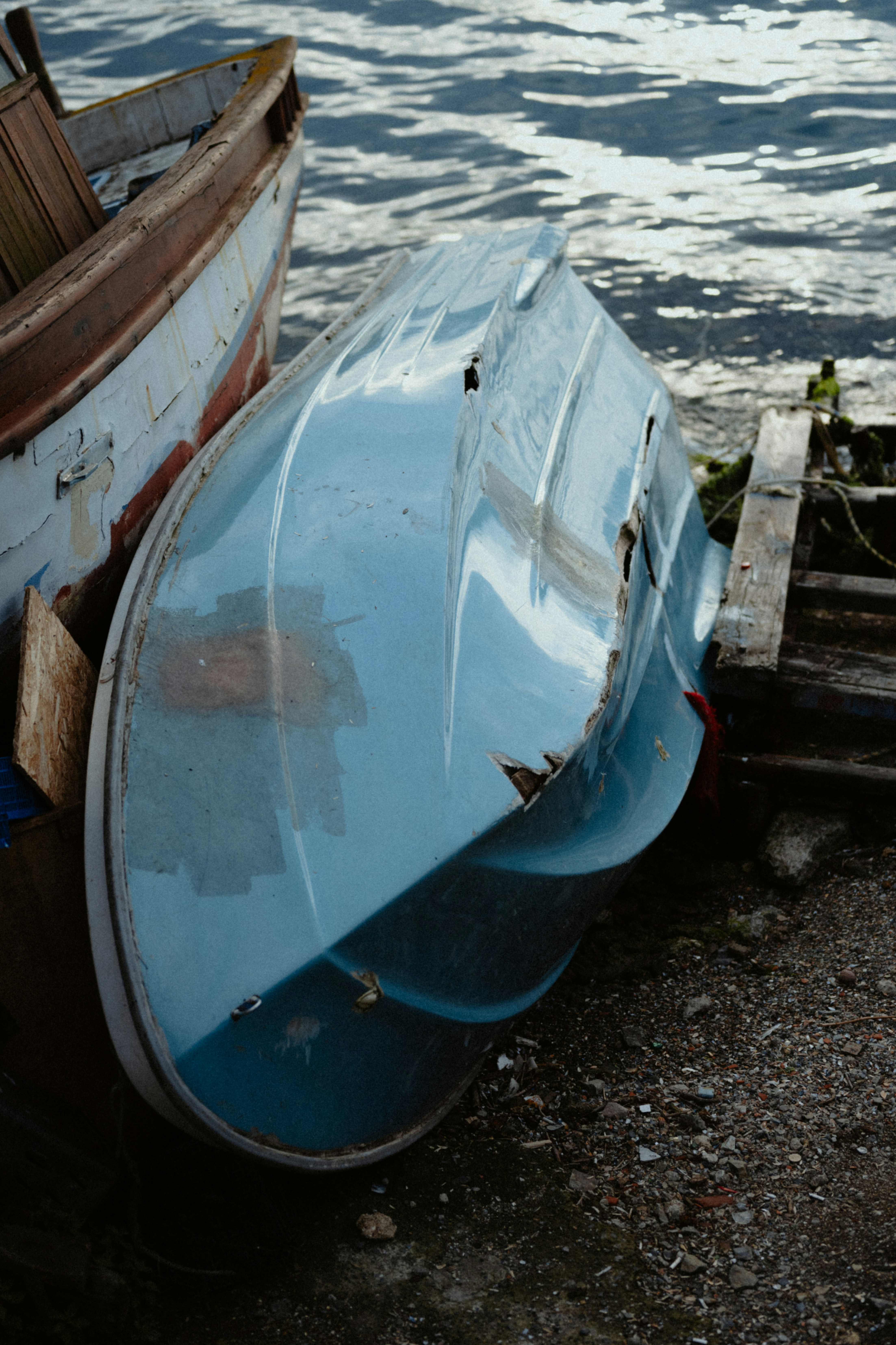 Perahu biru lapuk terbalik di pantai di tepi air.