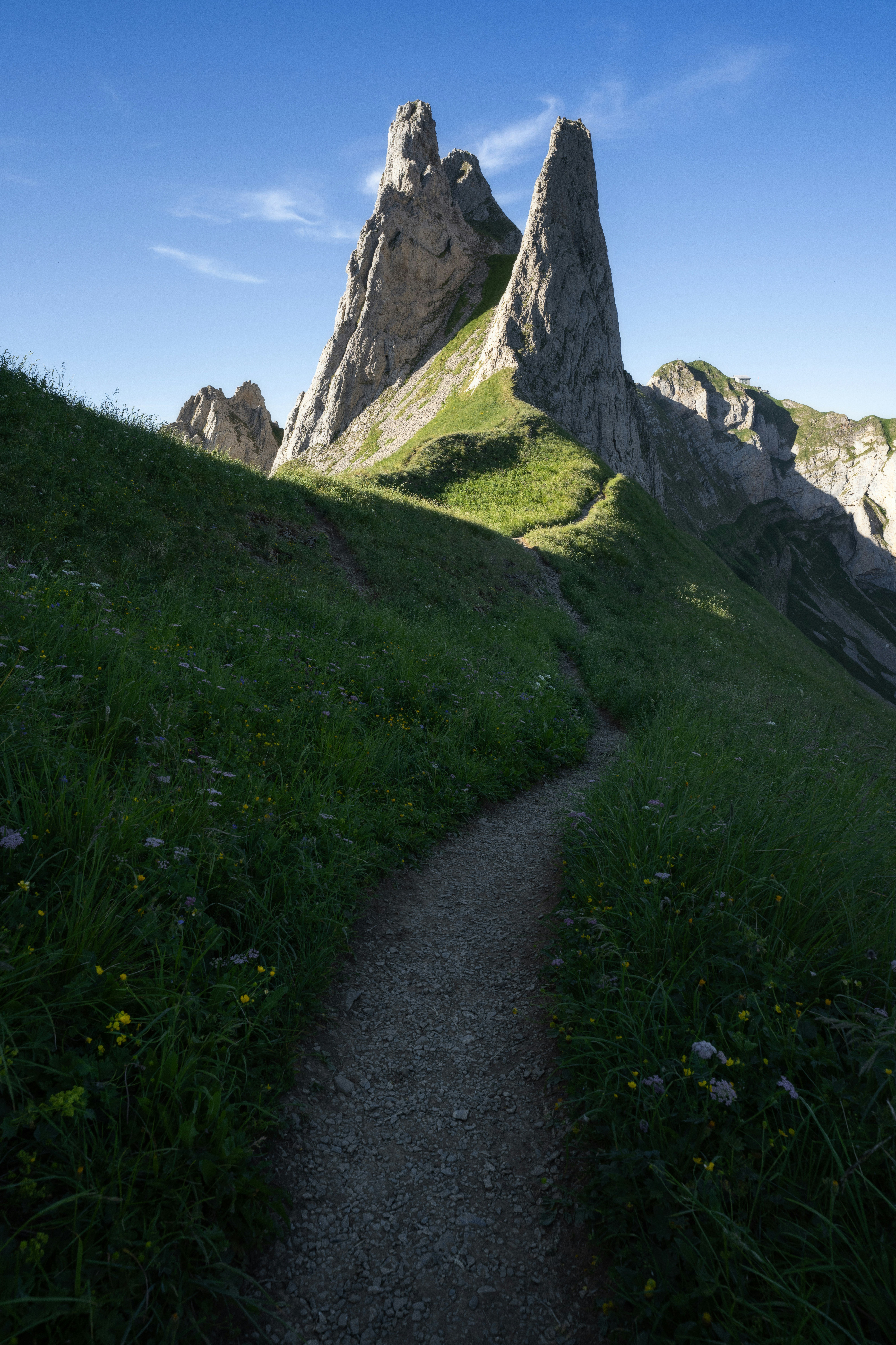 A winding path leads through green mountains to jagged peaks.
