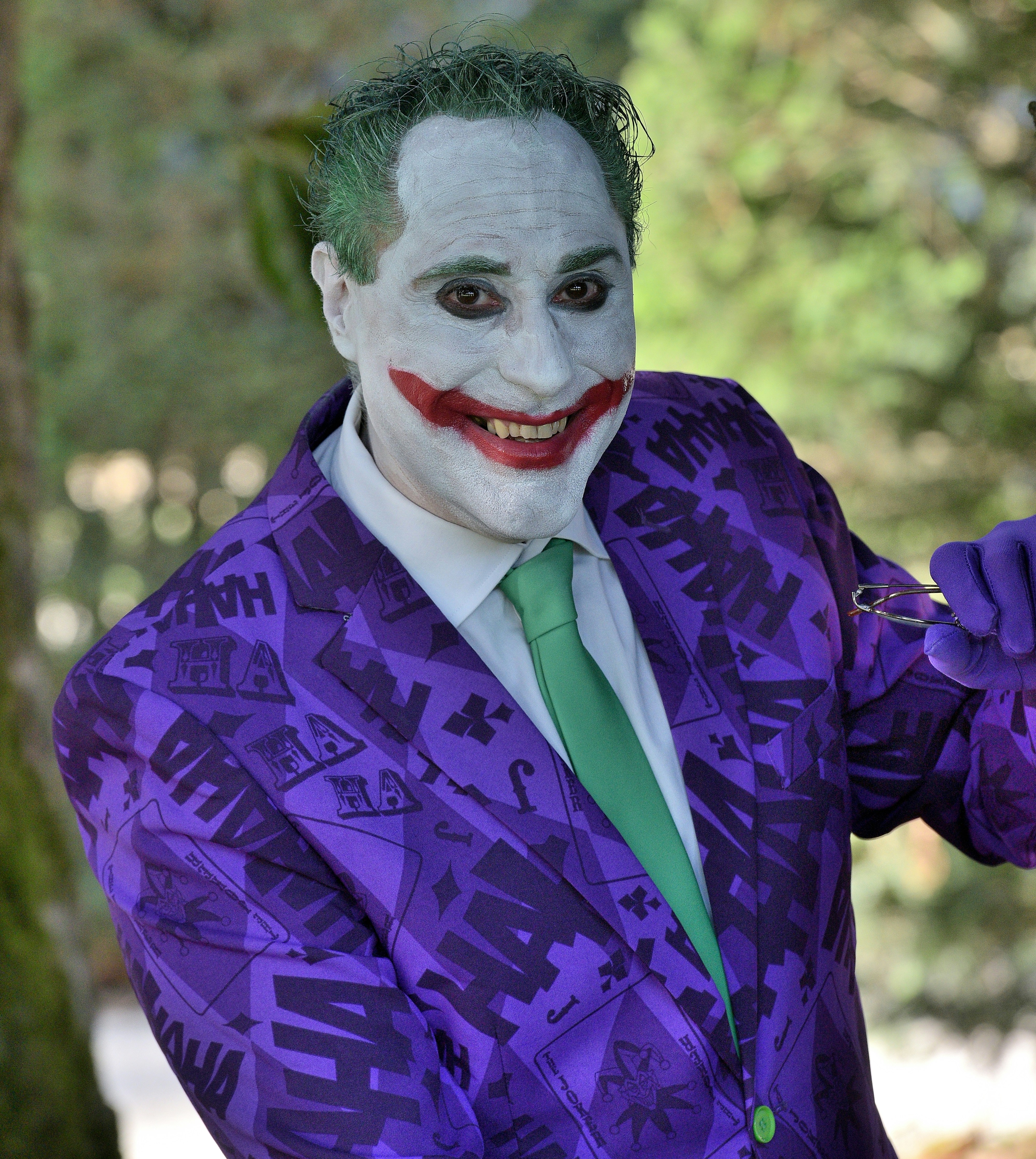 A smiling man dressed as the joker with purple suit.