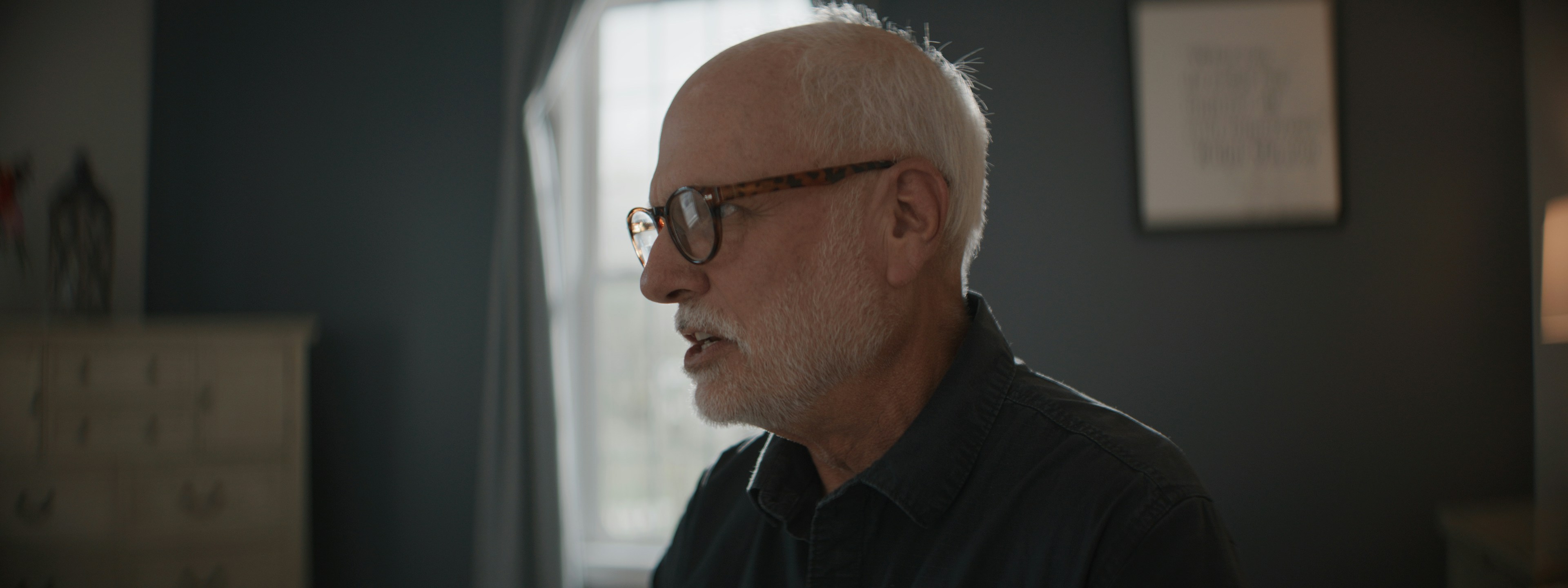 Elderly man with glasses and beard looking left indoors