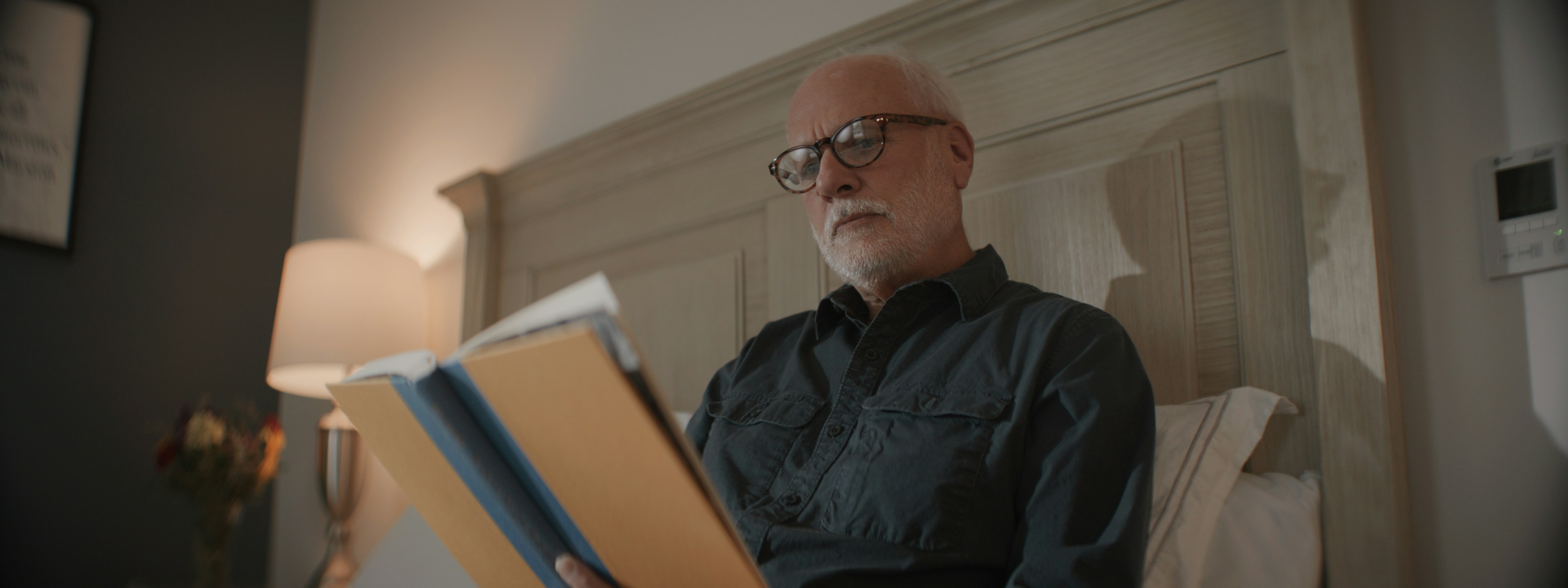 Senior man with glasses reading documents in bed.