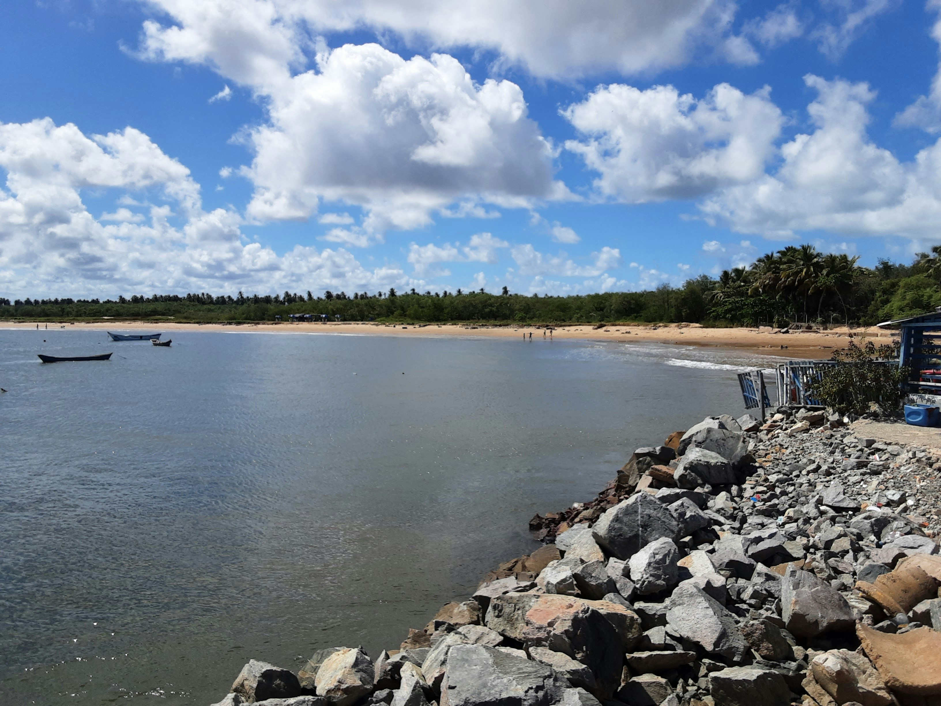 Calm water with boats, sandy beach, and rocky foreground