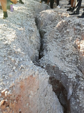 A narrow trench cut through dry rocky ground, similar to the caliche soil common across the Las Vegas valley