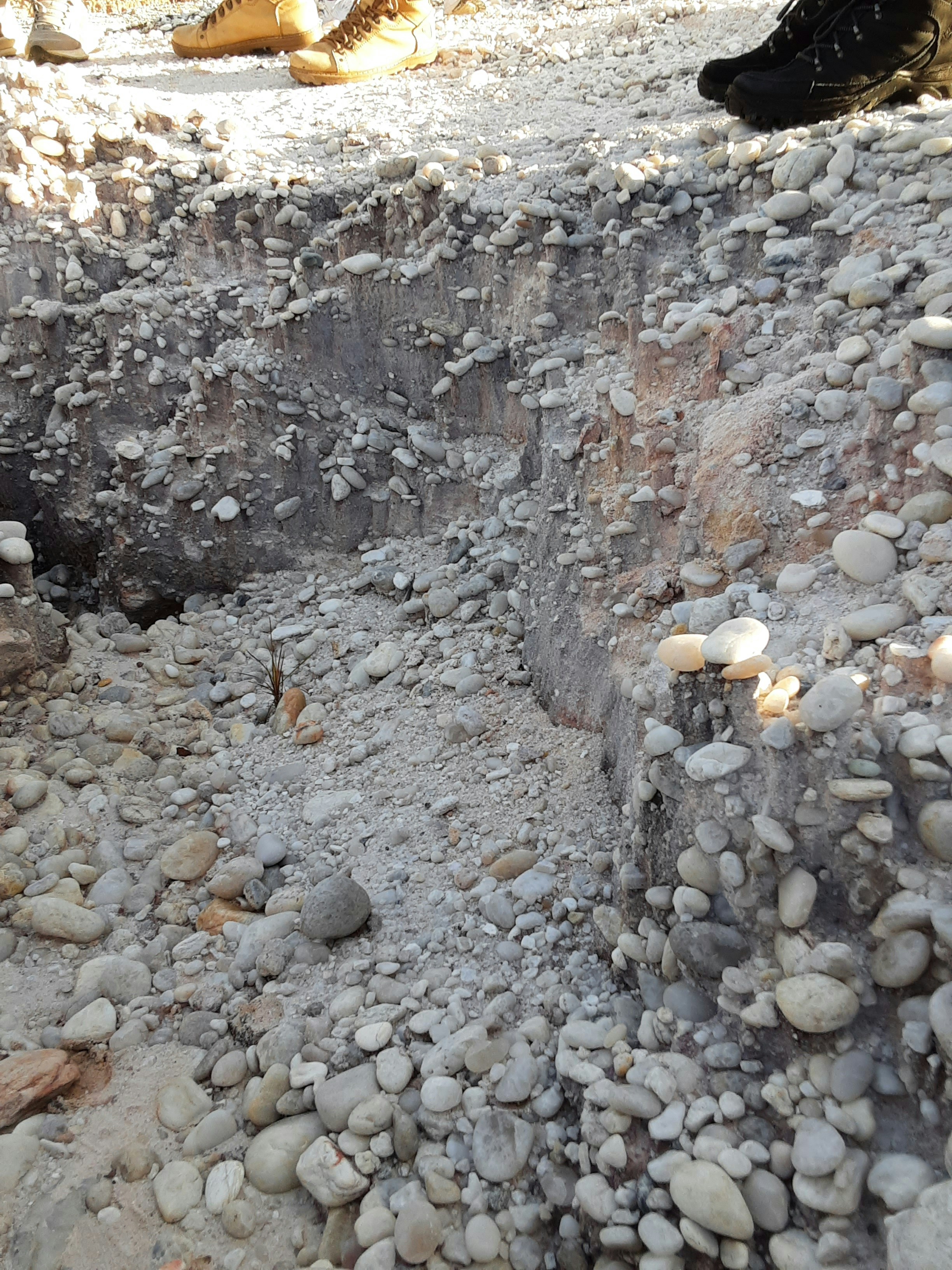 Excavated trench revealing layers of rocky, gravelly soil.