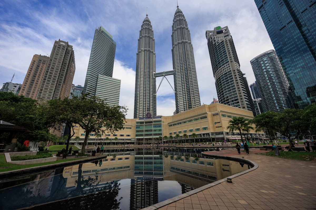Petronas Twin Towers reflected in a pool beside a park footpath on an overcast day