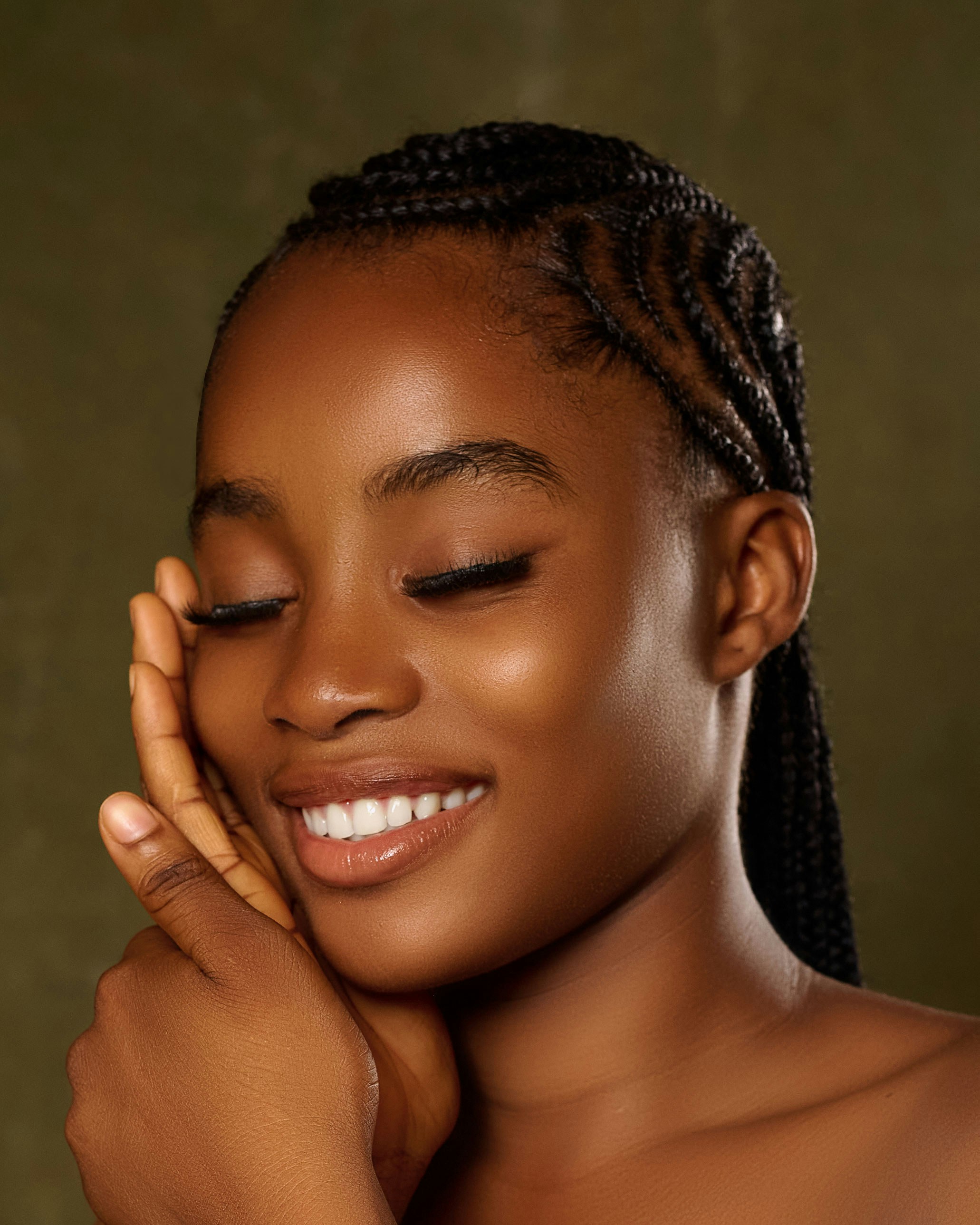 Jeune femme souriante, aux cheveux tressés et aux yeux fermés.