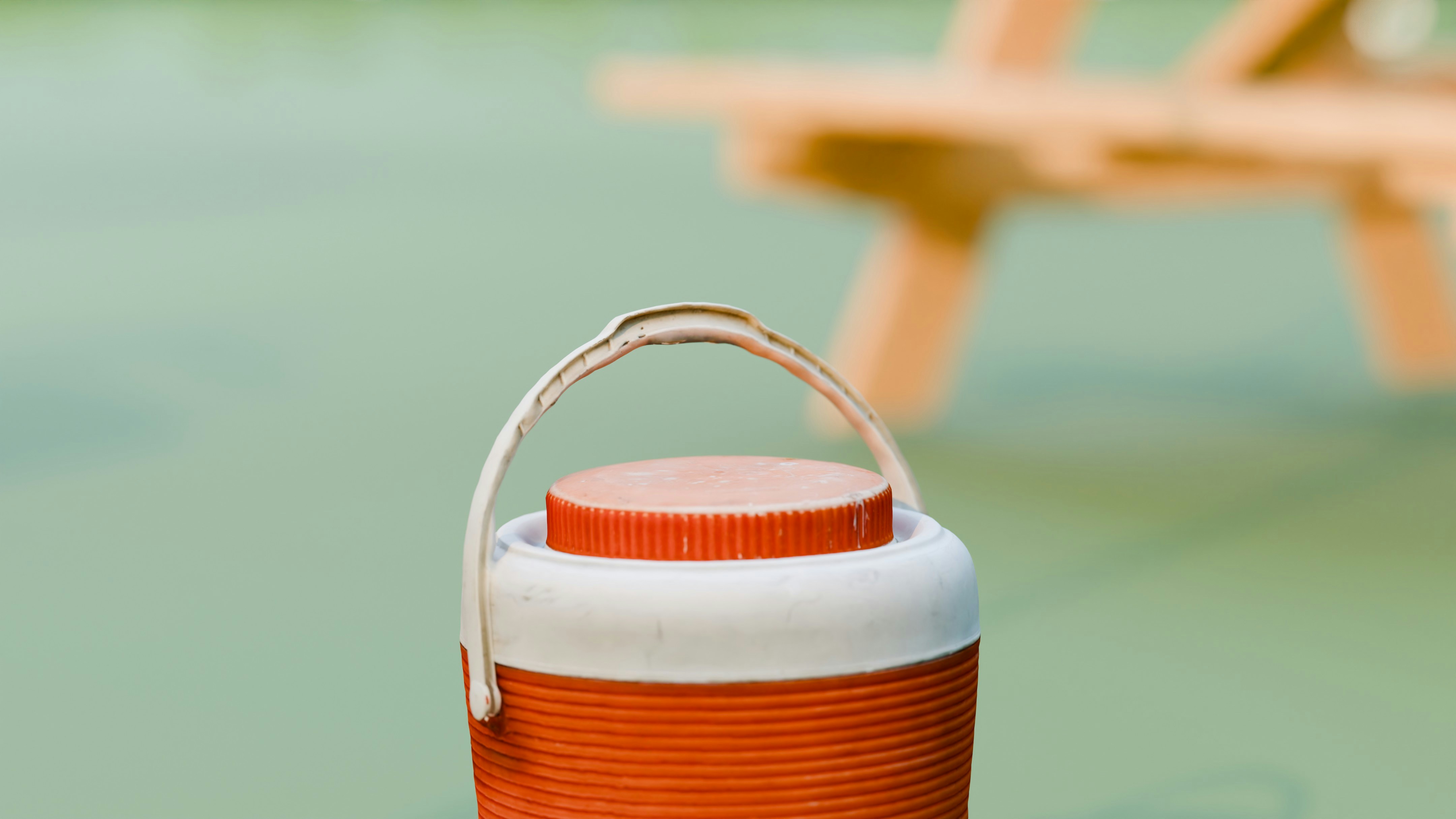 An orange and white cooler sits on green ground outdoors.