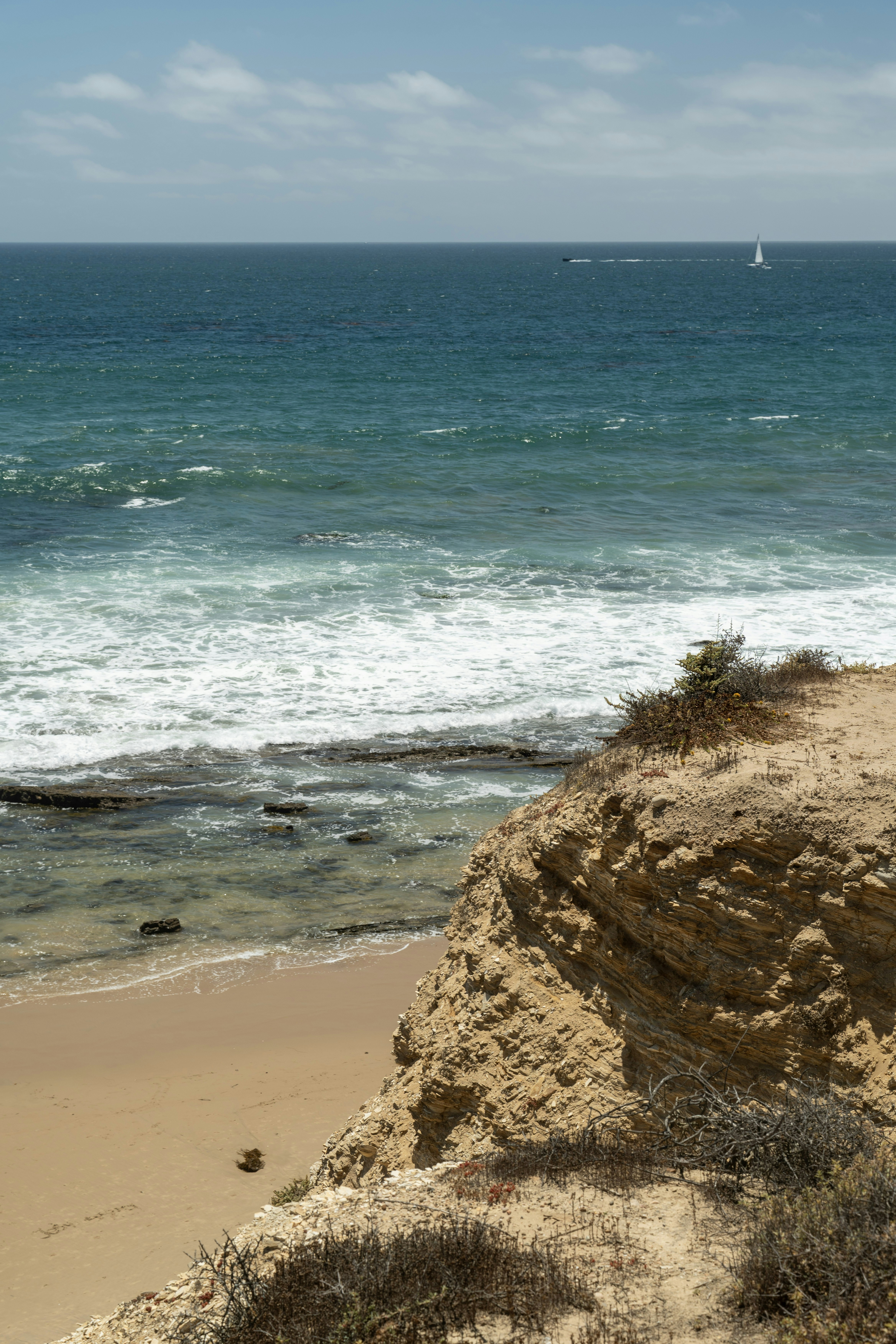 Rocky cliff overlooks a sandy beach and blue ocean.