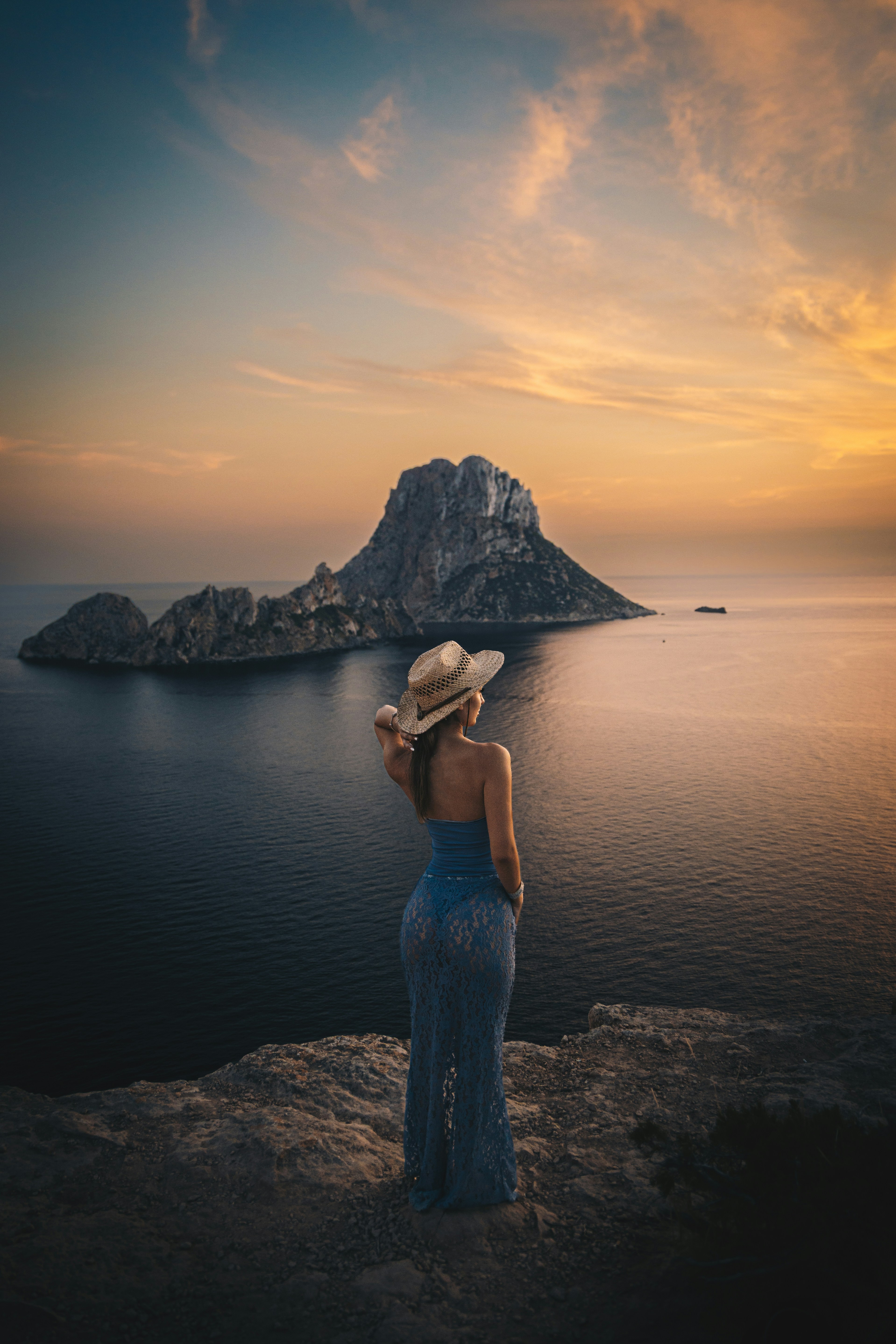 Woman in hat admiring sunset over a rocky island