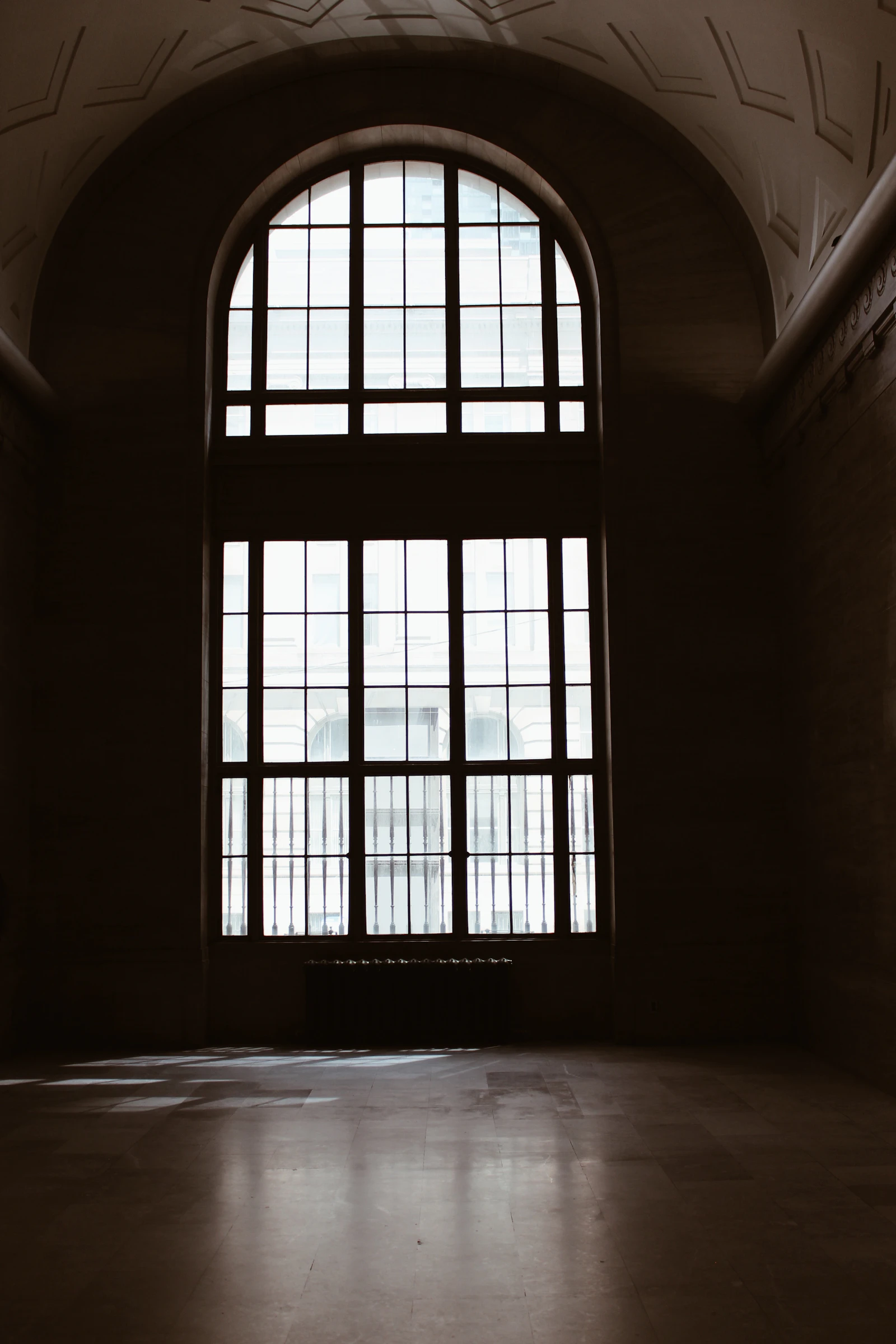 A tall arched window throwing light across the floor of a dark empty room