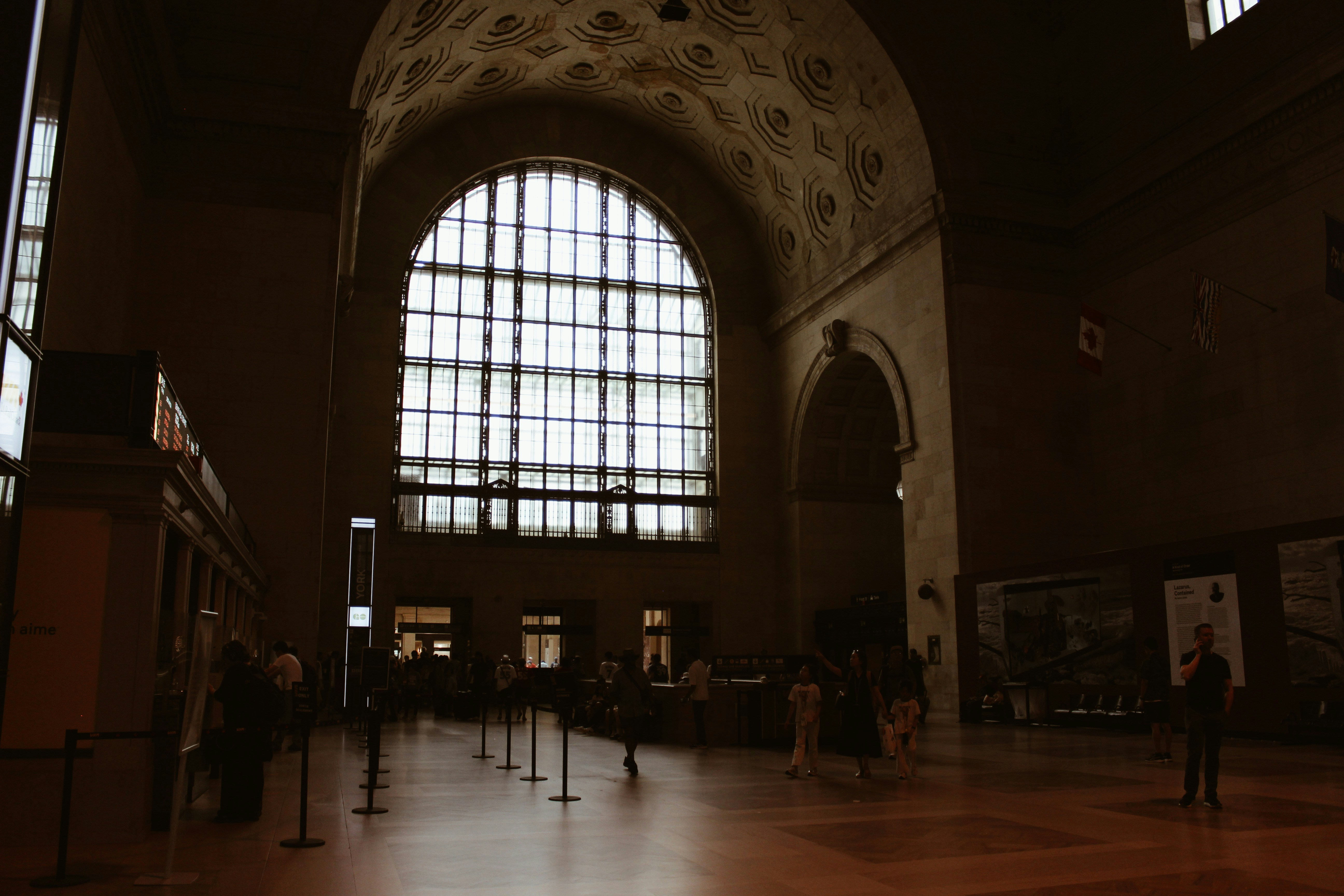 Grand hall with a large arched window and scattered people.